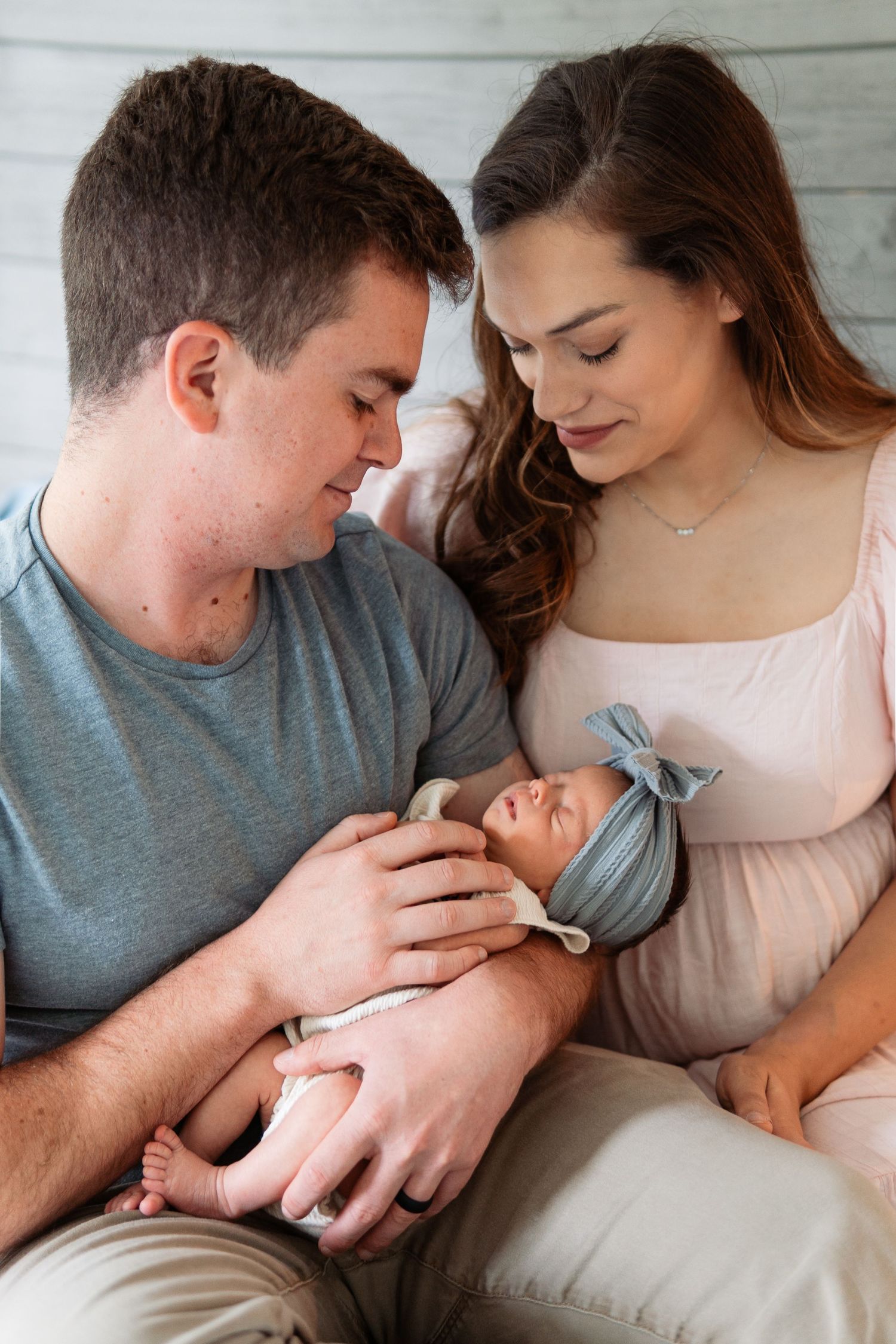 Parents cuddling with their newborn baby on a cozy bed in gentle natural light.