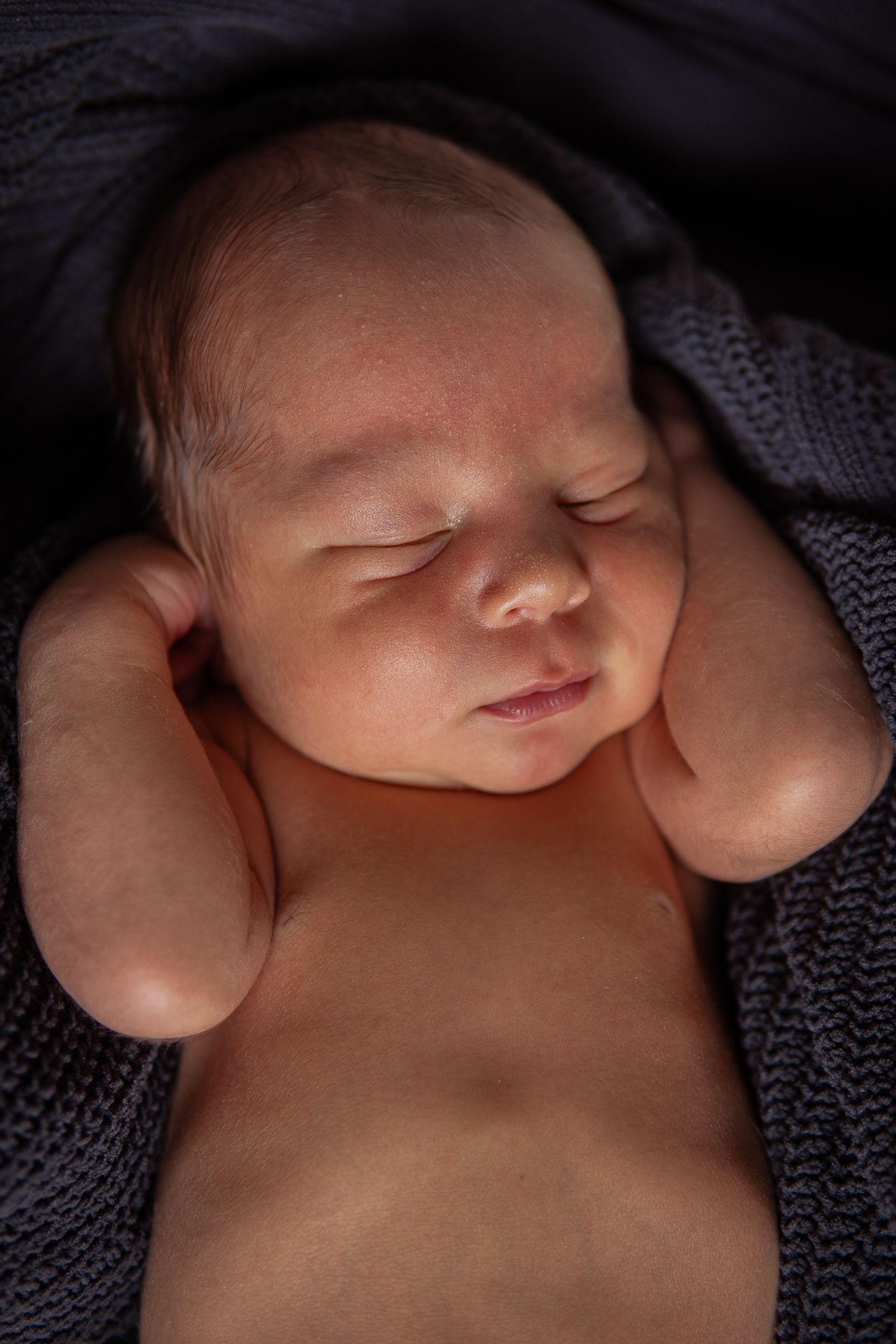 Peaceful newborn baby sleeping wrapped in soft dark knitted blanket.