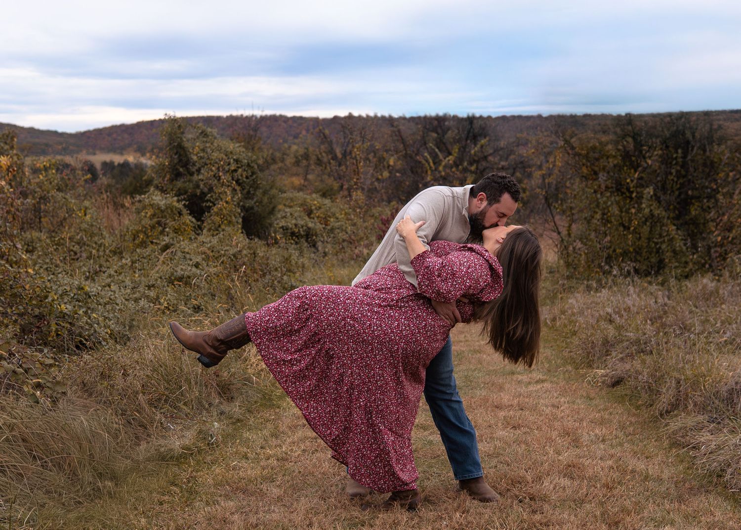 Romantic couple sharing a passionate dip kiss on a scenic autumn mountain trail.