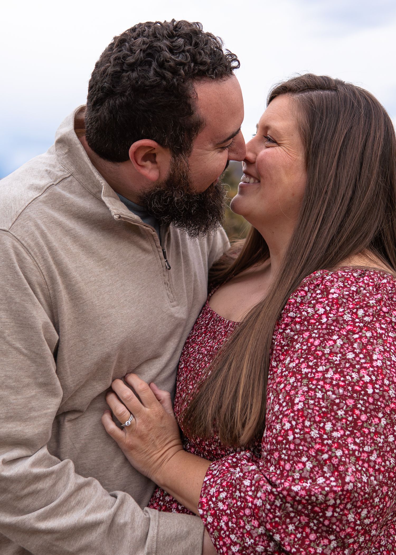 Bearded man and woman sharing a tender nose-to-nose moment, woman wearing red floral dress.