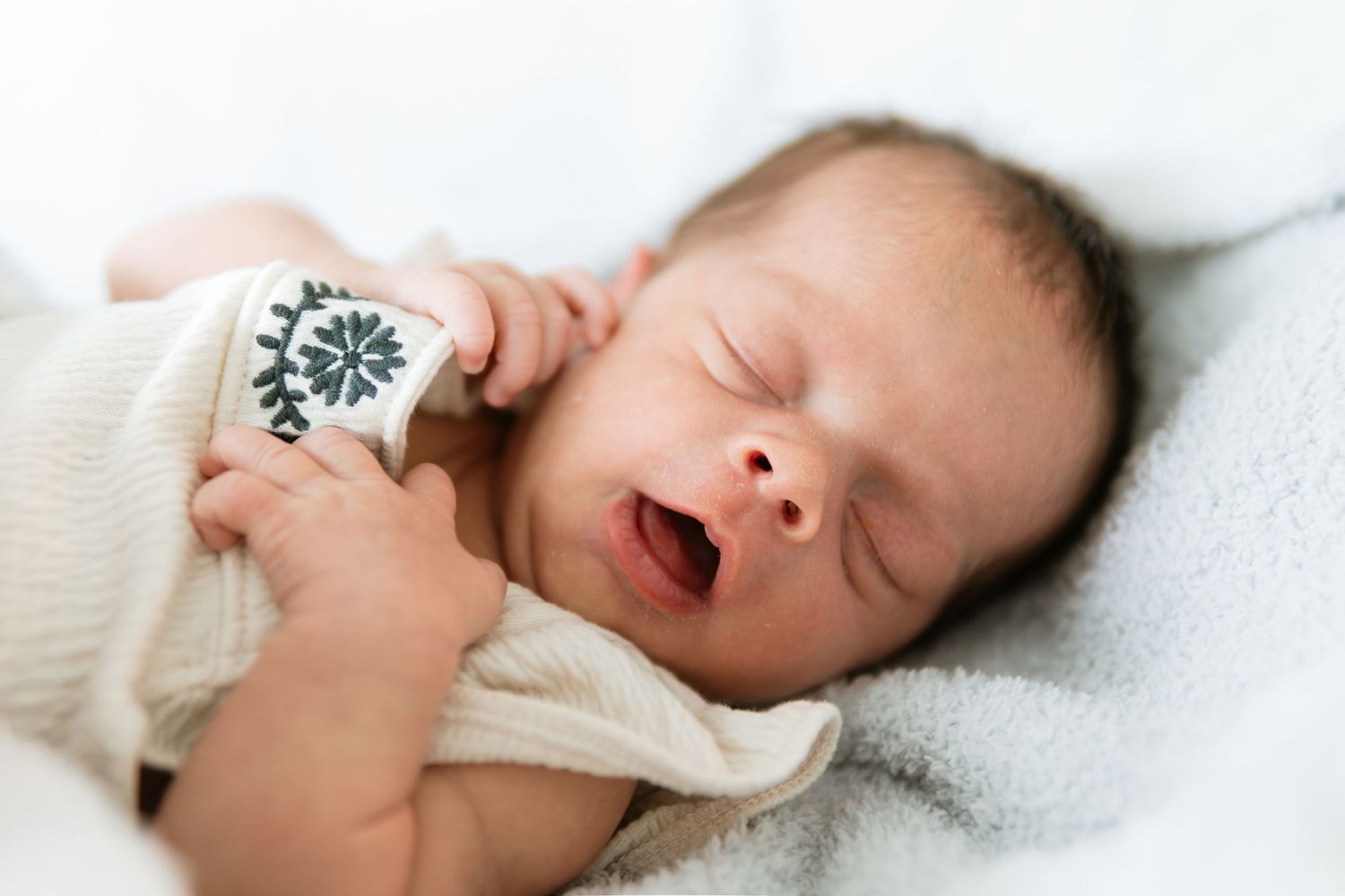 Infant yawning while resting on white bedding.