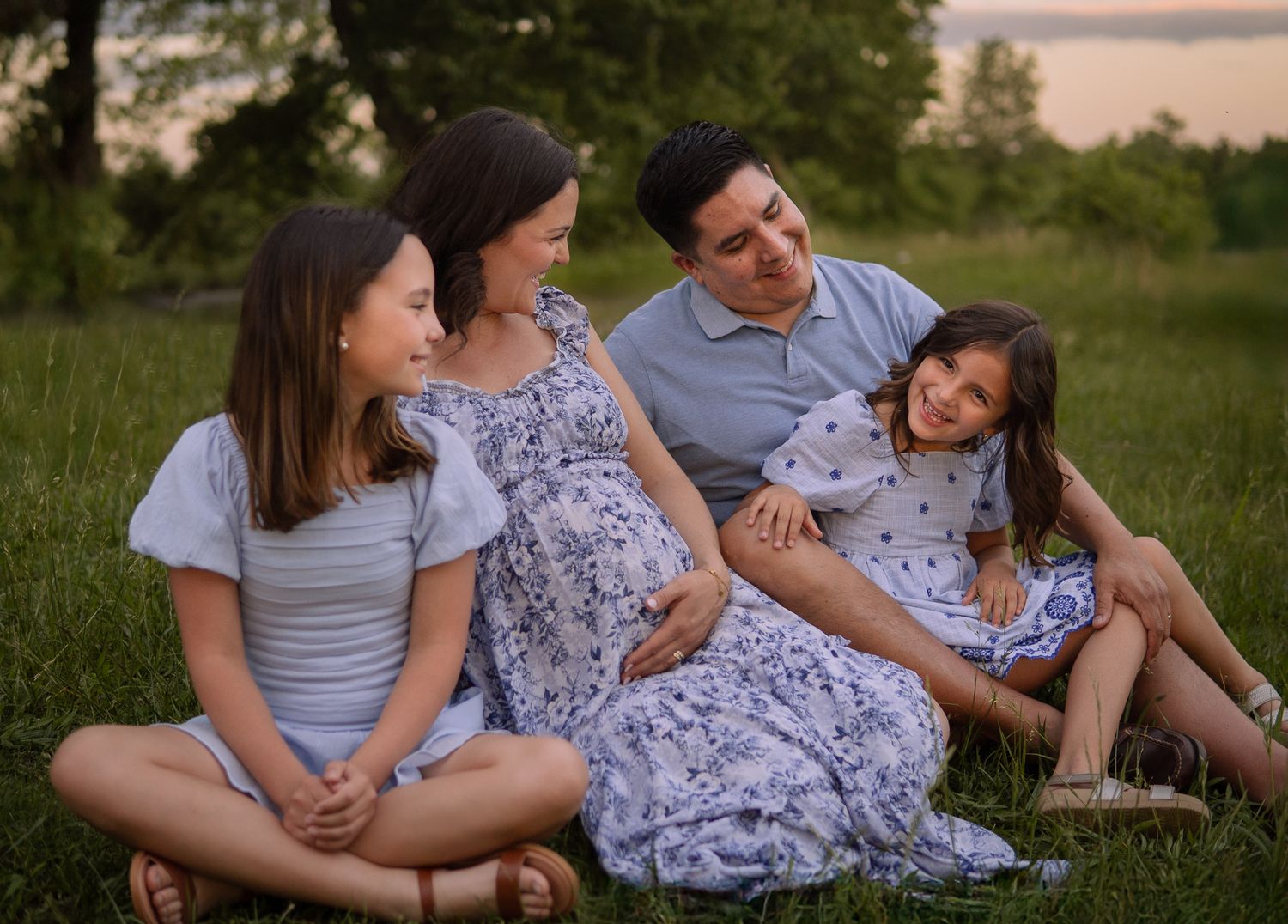 A family sits together on grass during sunset, sharing a tender moment outdoors.