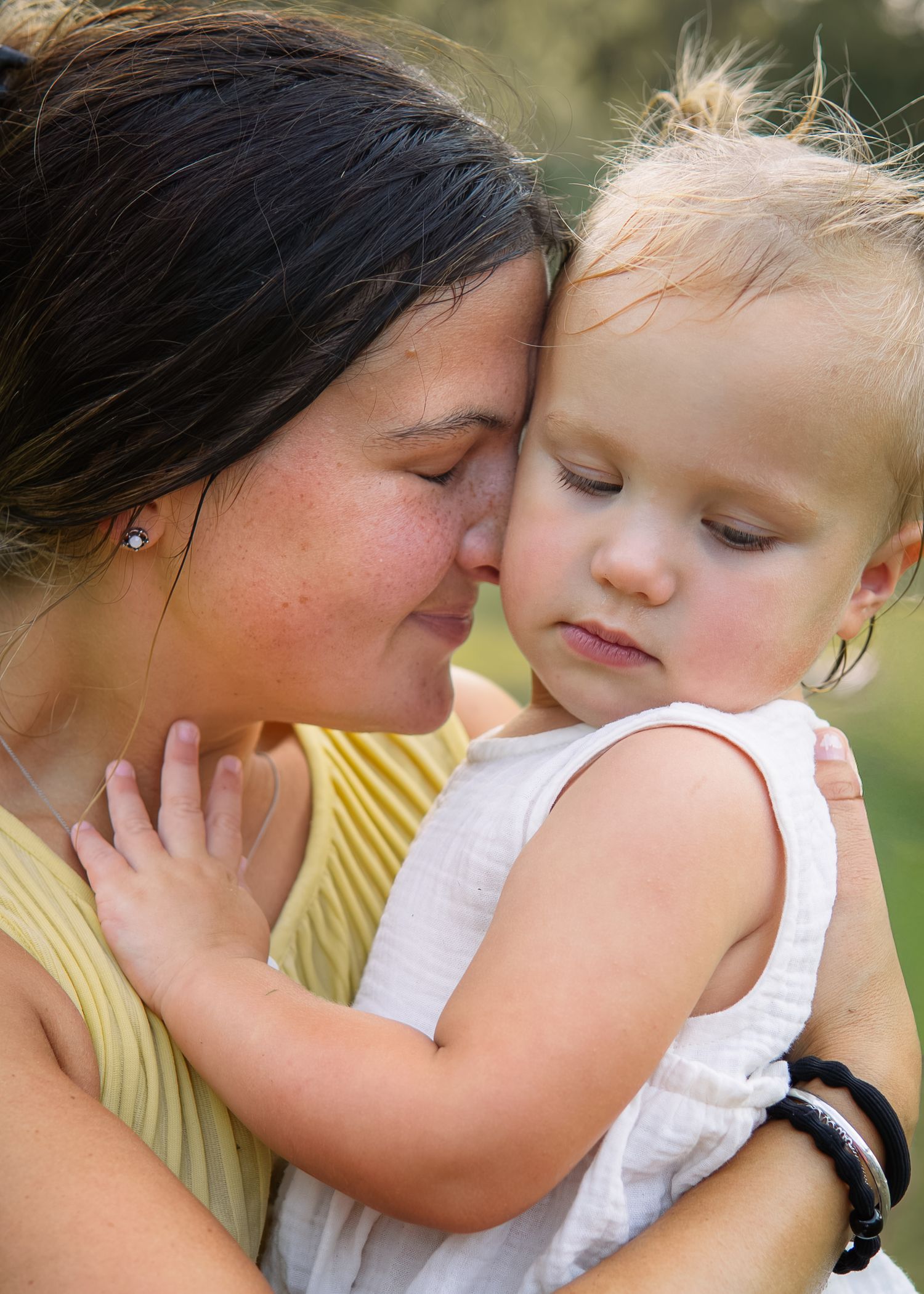 A tender moment as a dark-haired mother presses her cheek lovingly against her sleepy toddler.