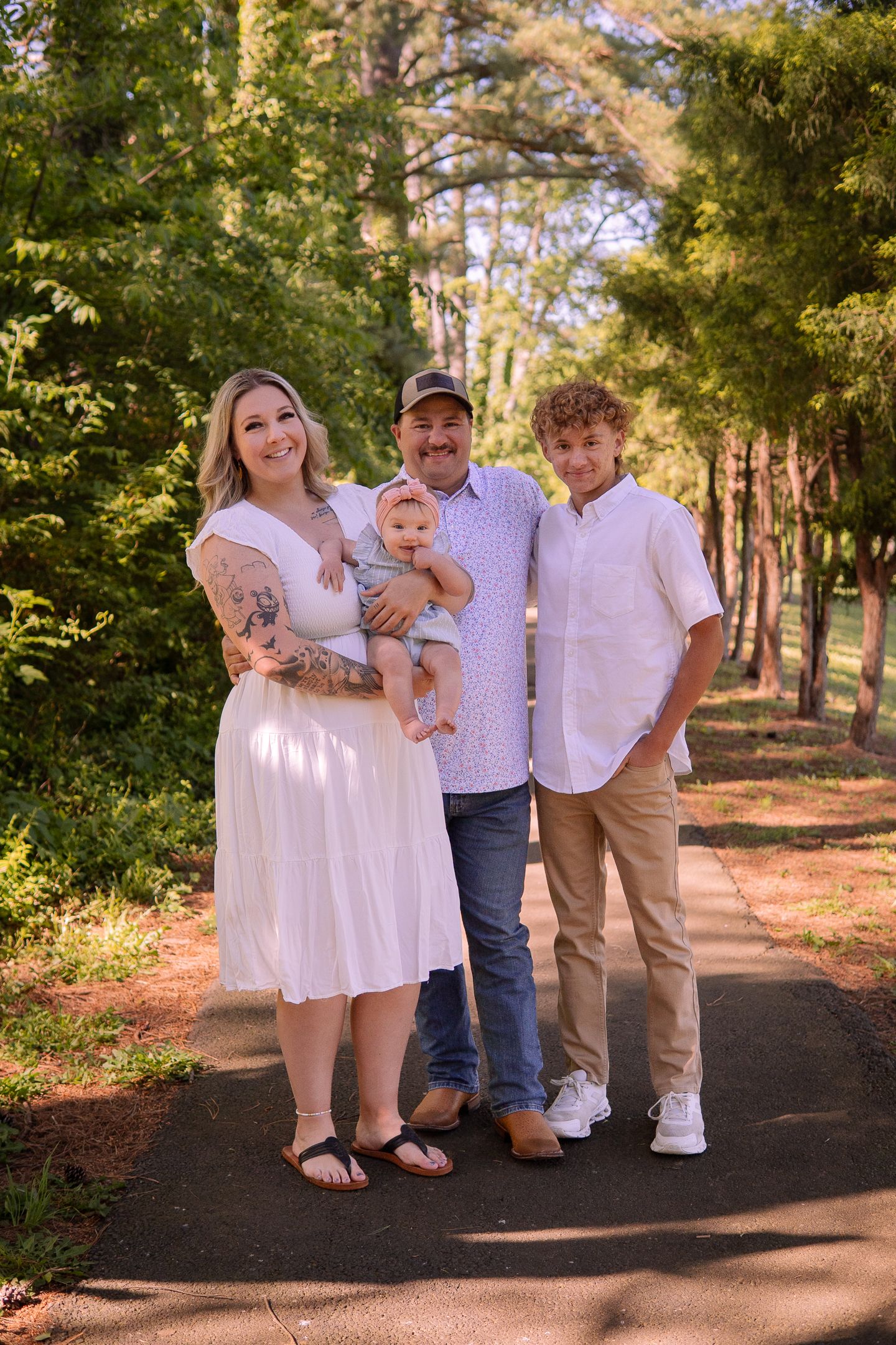 Family portrait on a tree-lined path showing coordinated white and neutral outfits in natural setting.