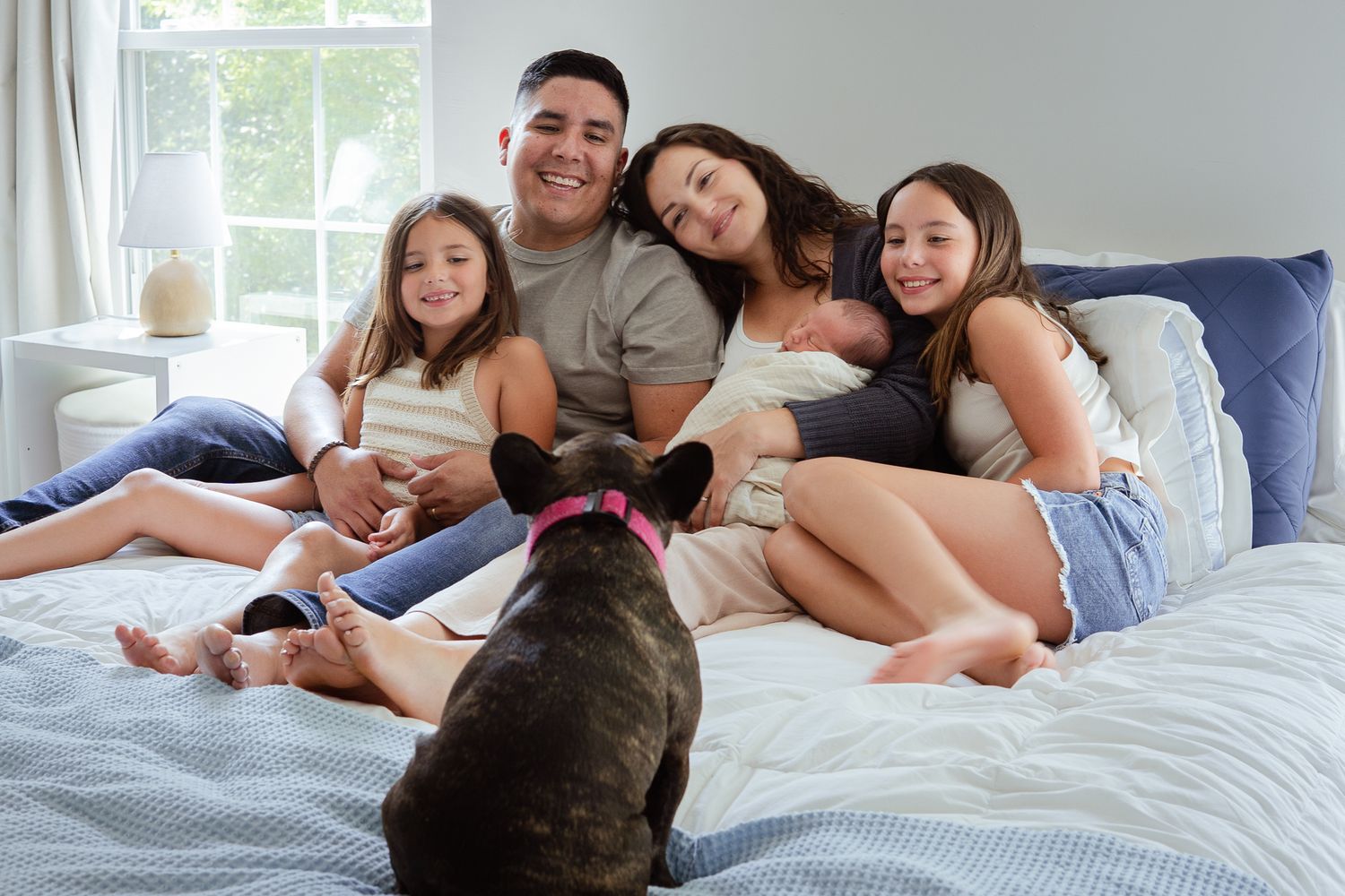 Happy family relaxing on bed with dog while bonding with newborn baby.