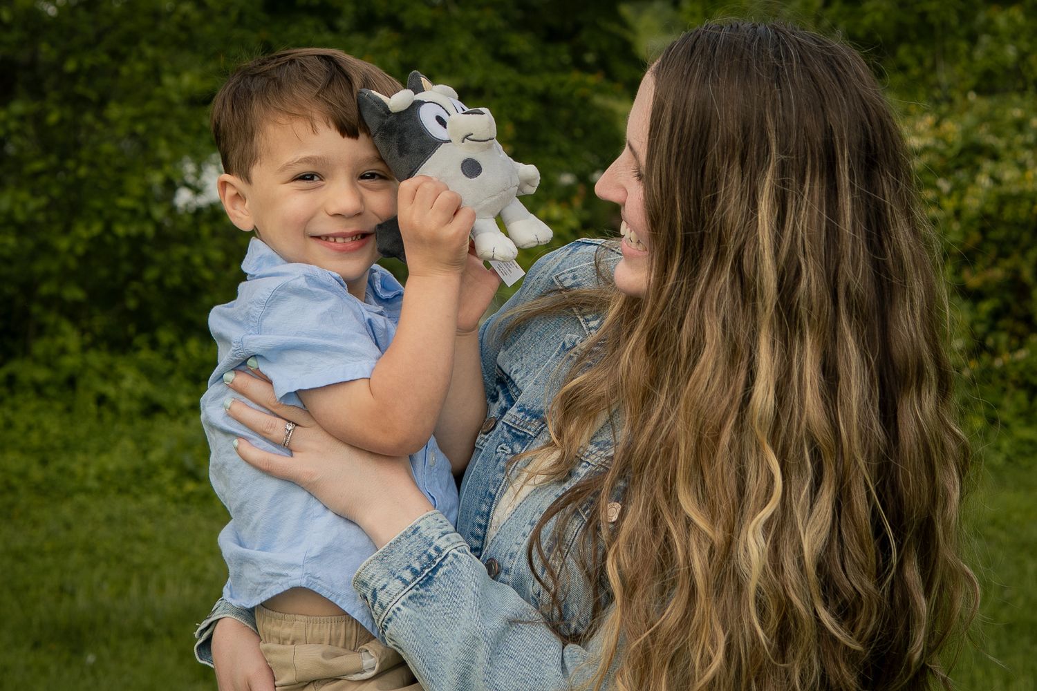 A child plays with a plush toy bunny while being held outdoors in a grassy area during daytime.