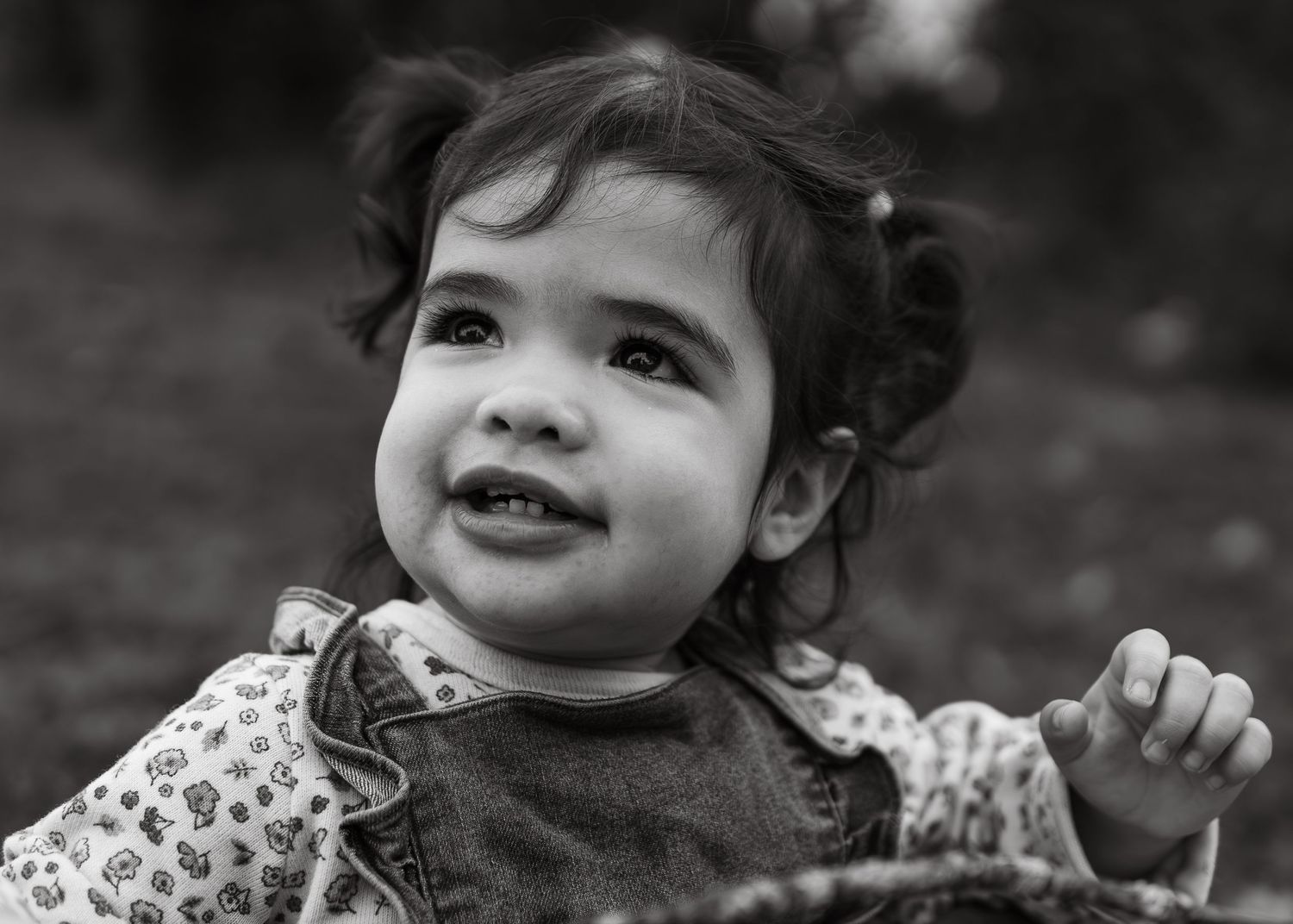 Black and white close-up portrait of a happy baby girl smiling outdoors in natural light.