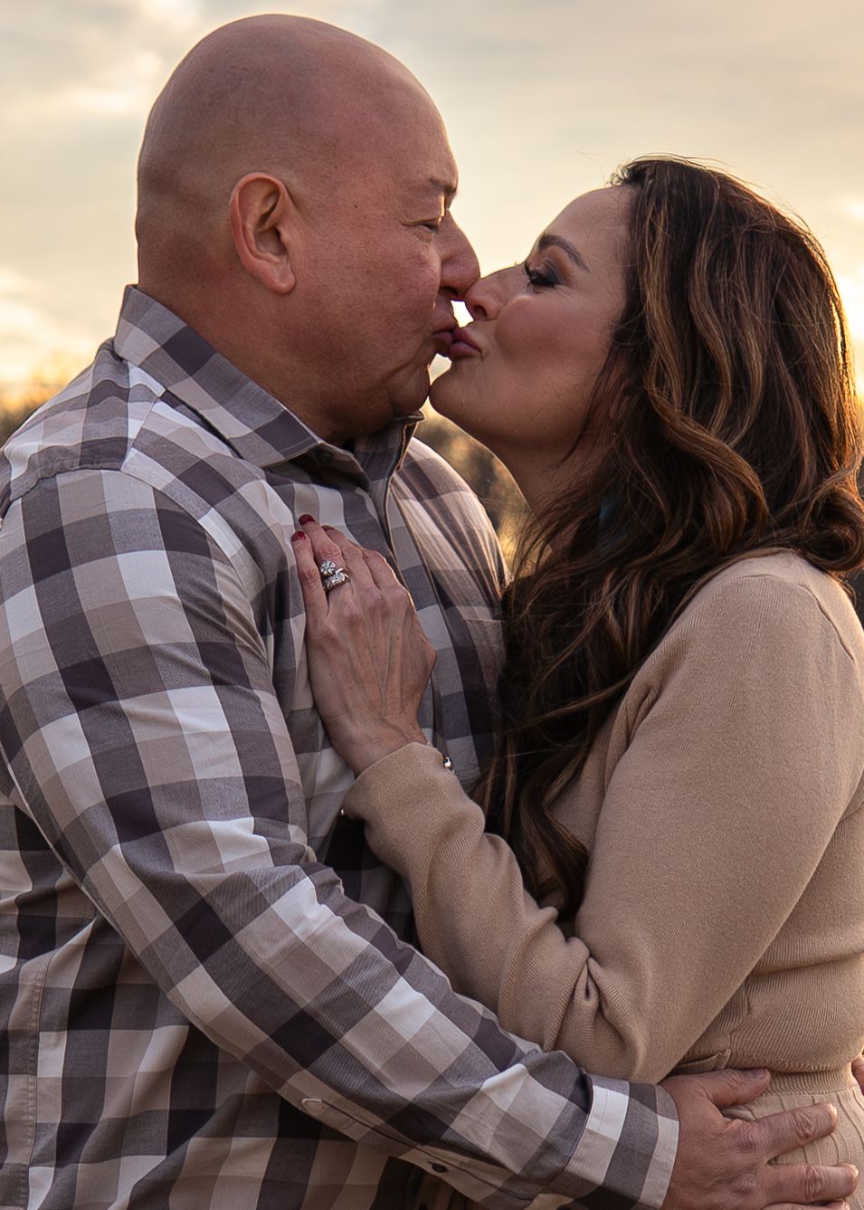 Couple sharing a passionate kiss outdoors at golden sunset, embracing romantically.