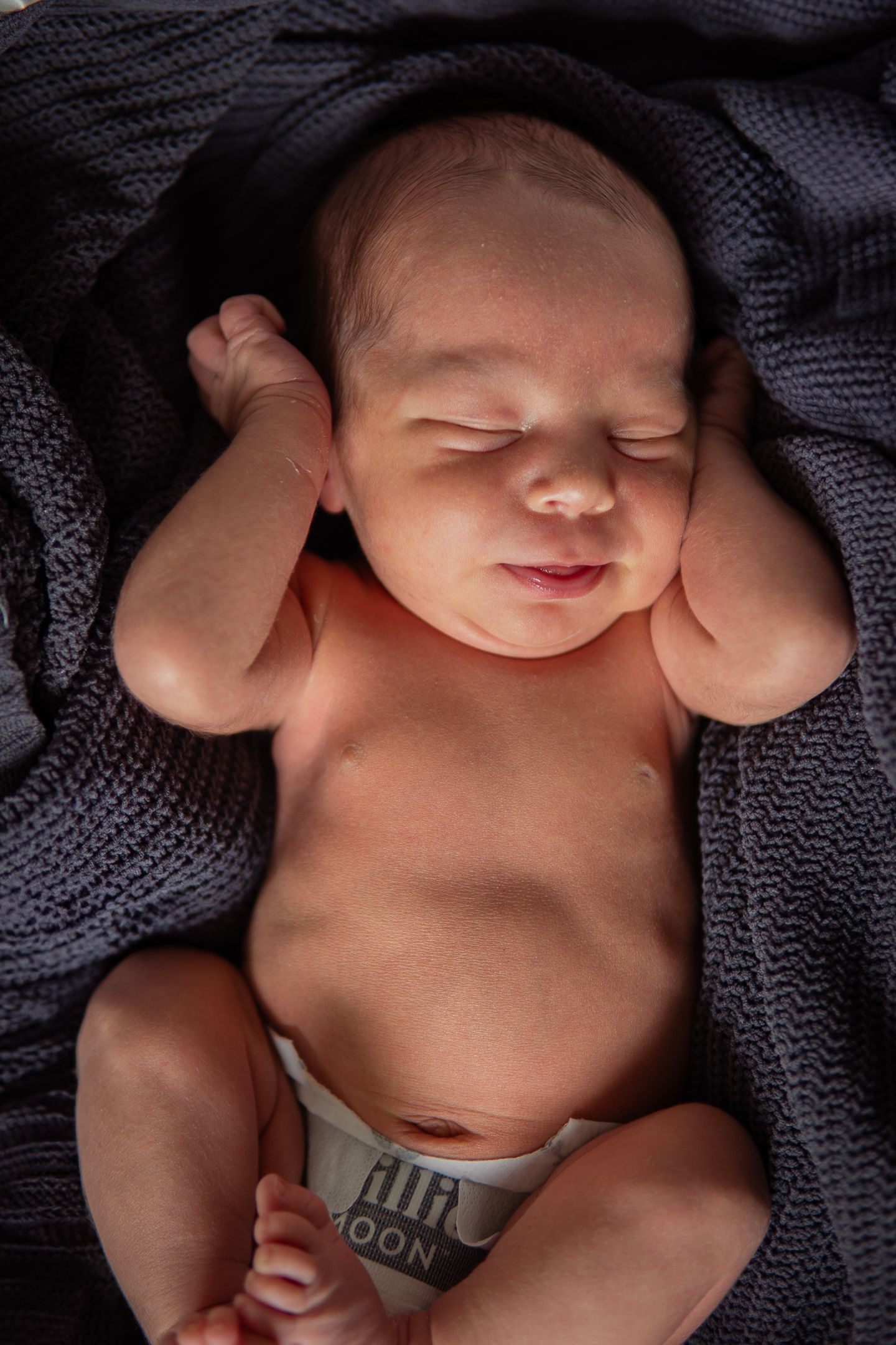 Close-up shots of peaceful sleeping infant wearing diaper under dark knit blanket.