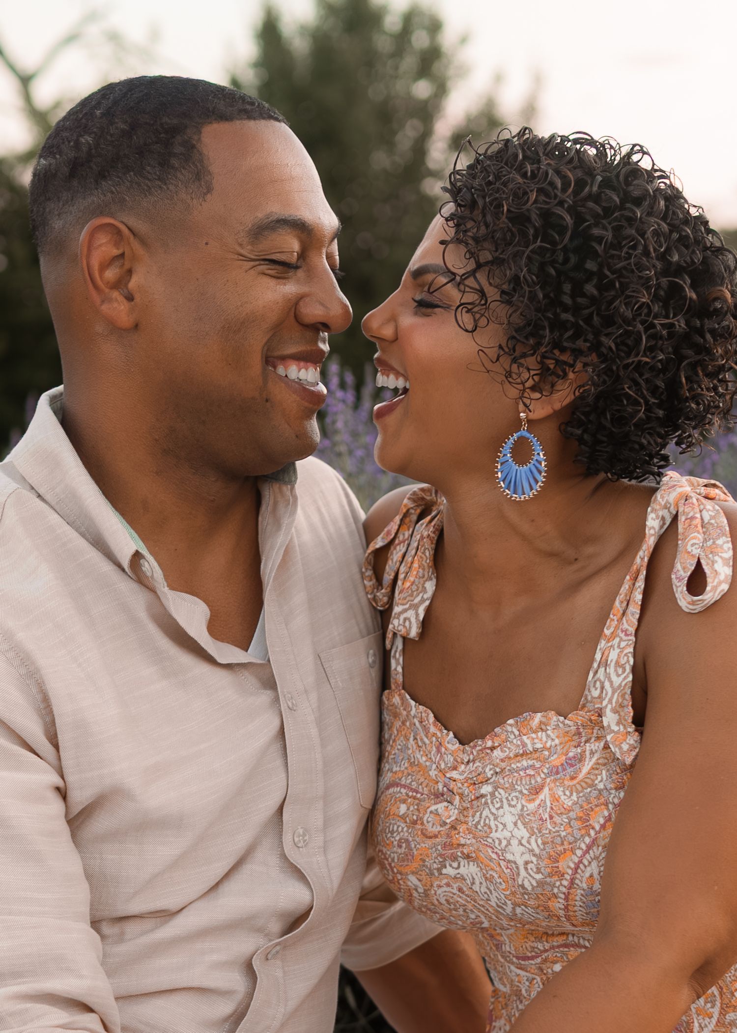 A joyful couple laughs together intimately in a blooming lavender field during a romantic outdoor photoshoot.