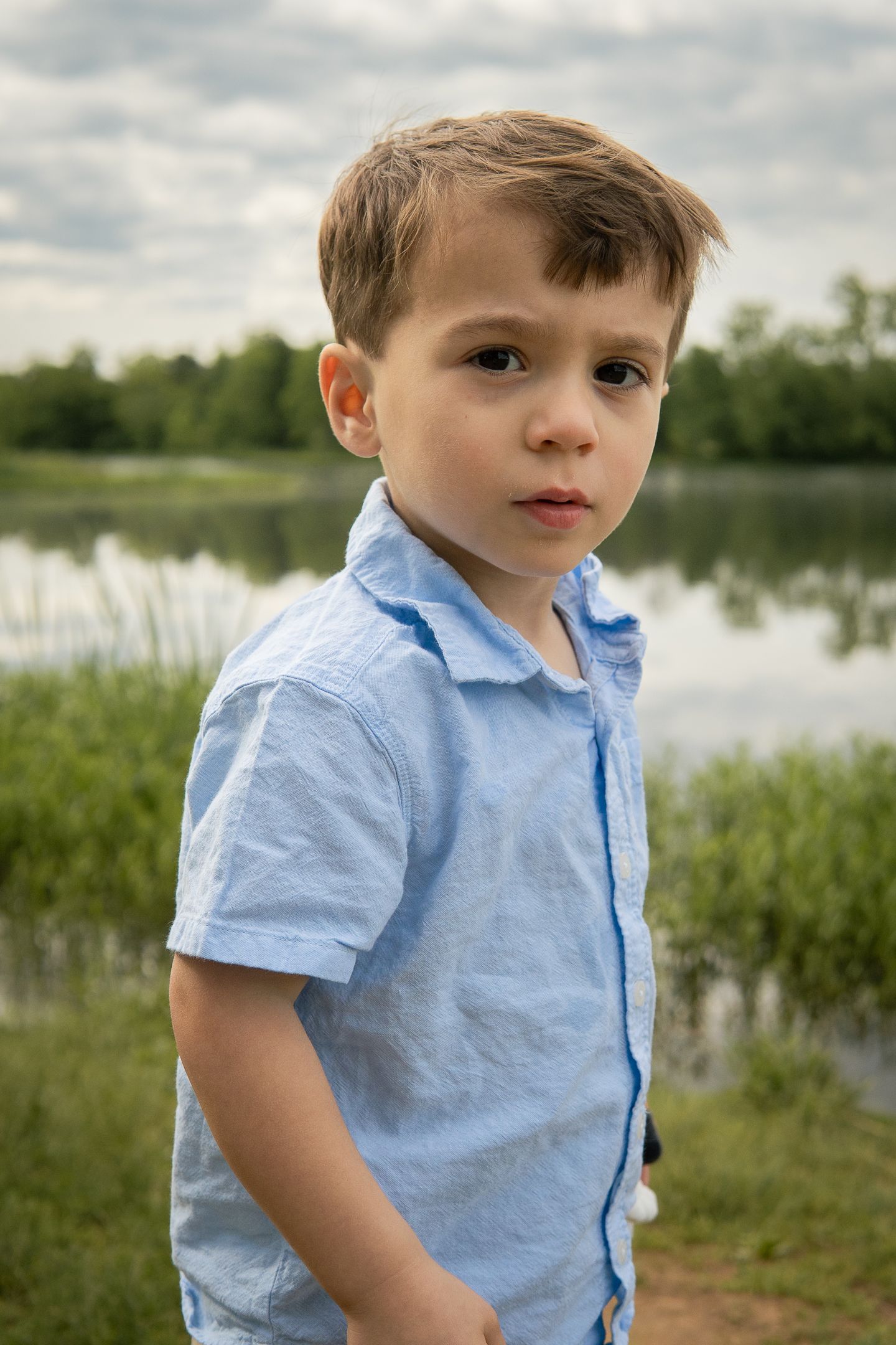 Series of portraits by a lake showing a young child in a light blue shirt against a natural background.