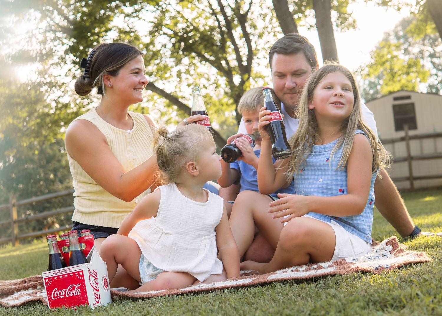 Family enjoying Coca-Cola drinks outdoors on a sunny day picnic on a blanket in a green park.