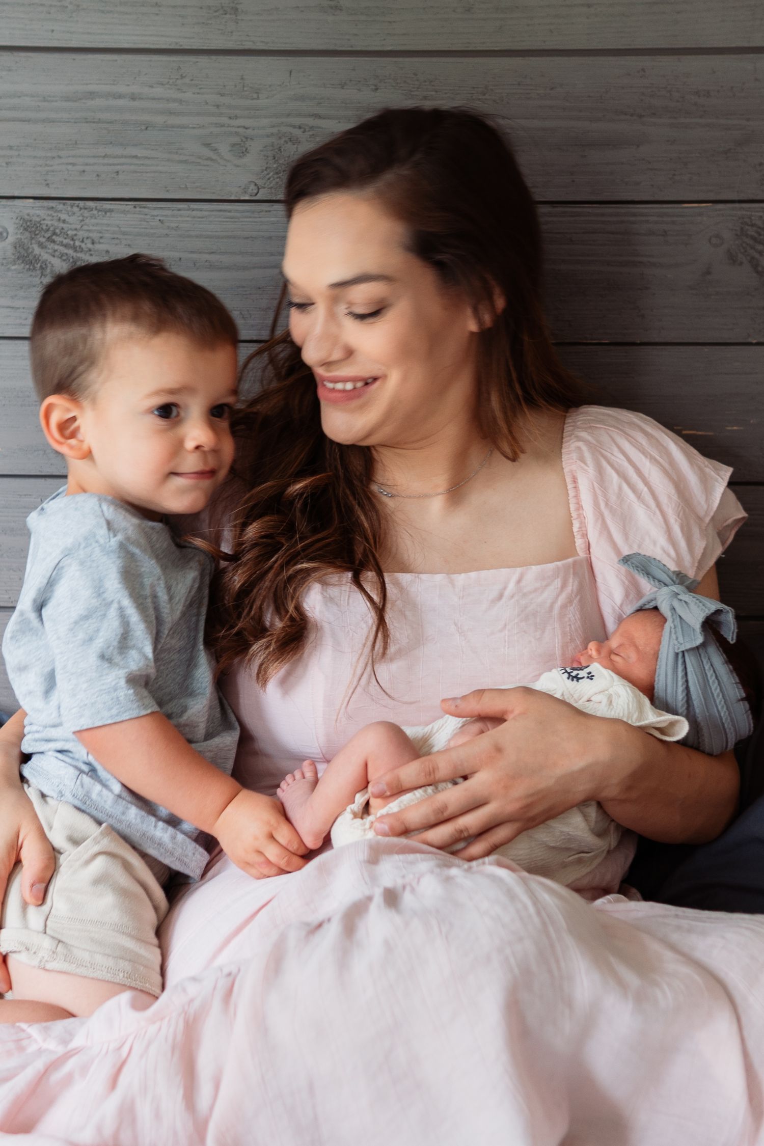 Family bonding with newborn in soft pastel colors against wooden backdrop.