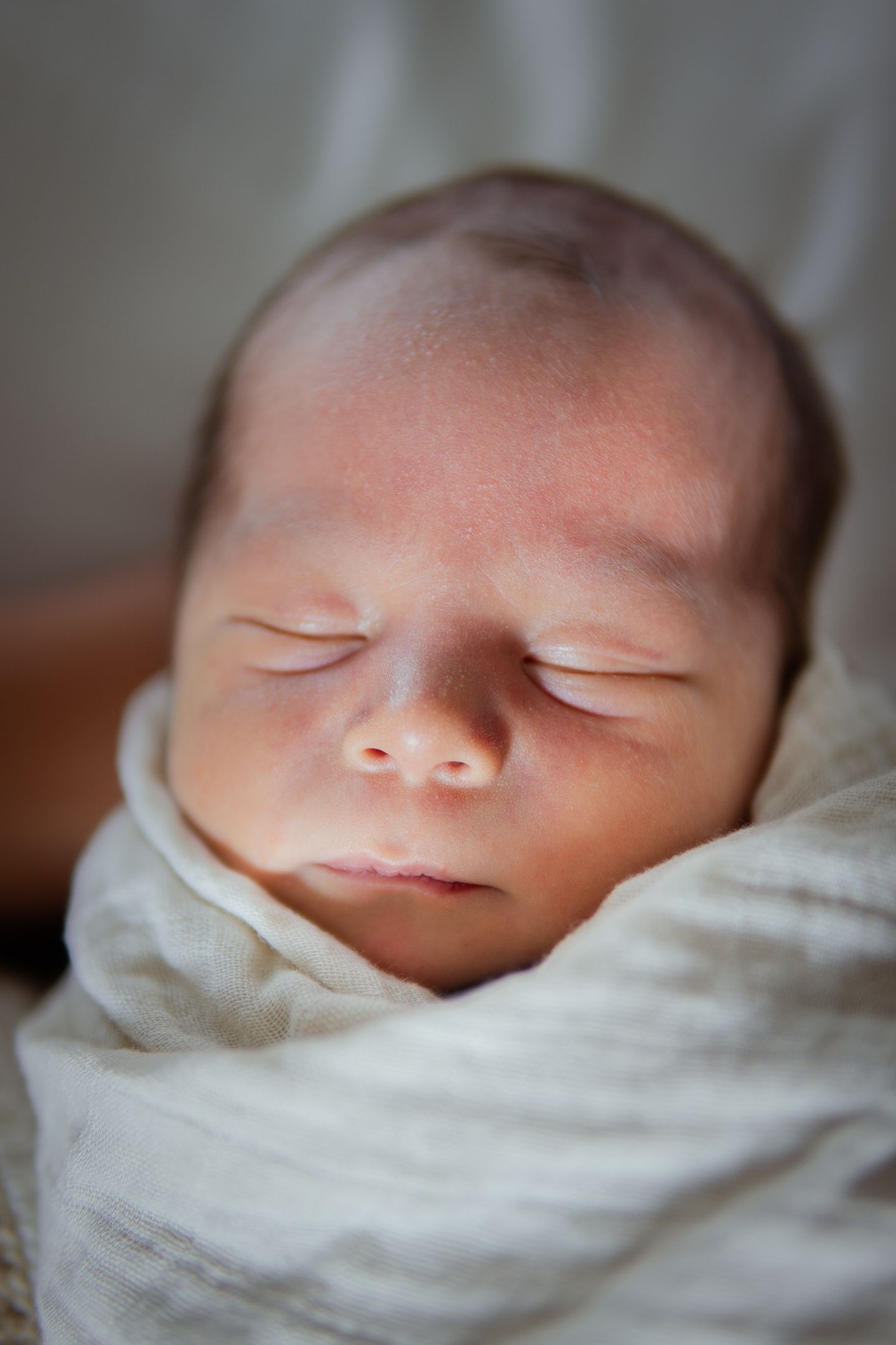 Peaceful sleeping newborn baby wrapped in soft white swaddle blanket.