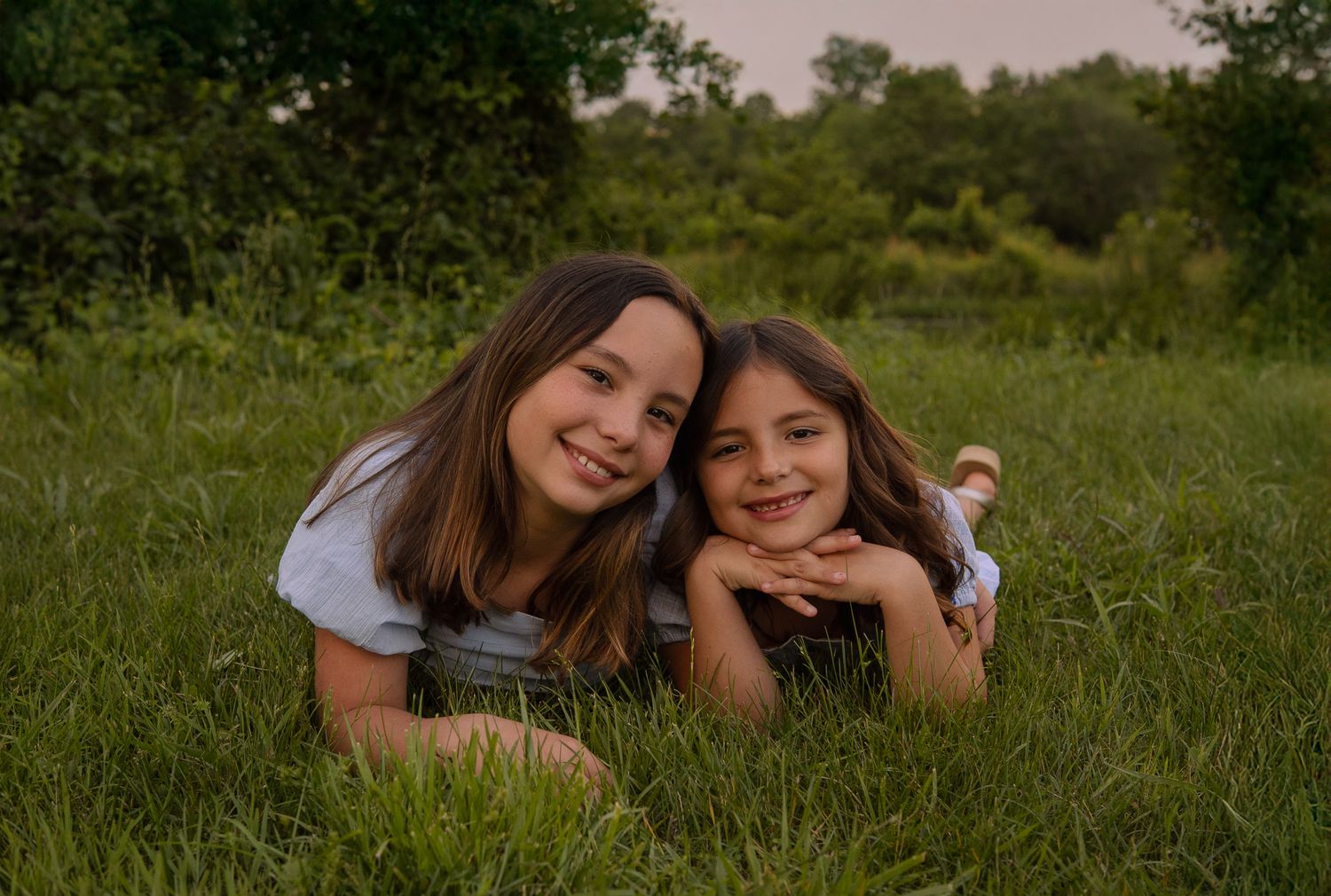 Two people lying in green grass on a sunny day sharing a cheerful moment in nature.