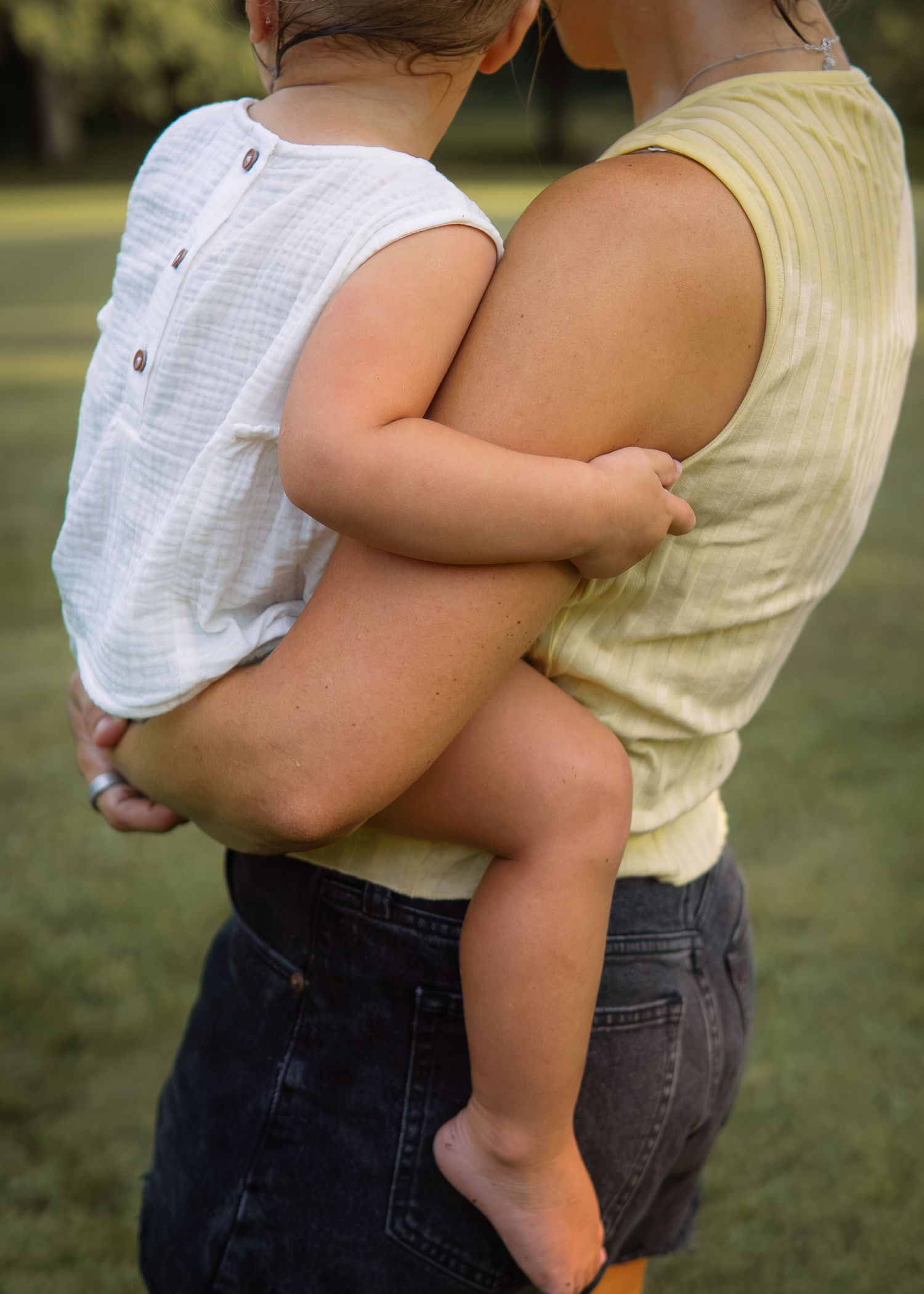 A close-up of a mother in a yellow top gently holding her young child against her shoulder outdoors.