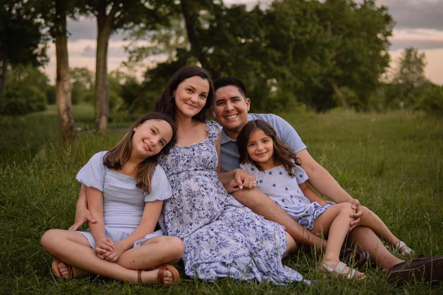 A family sits together on grass during golden hour creating a heartwarming outdoor portrait.