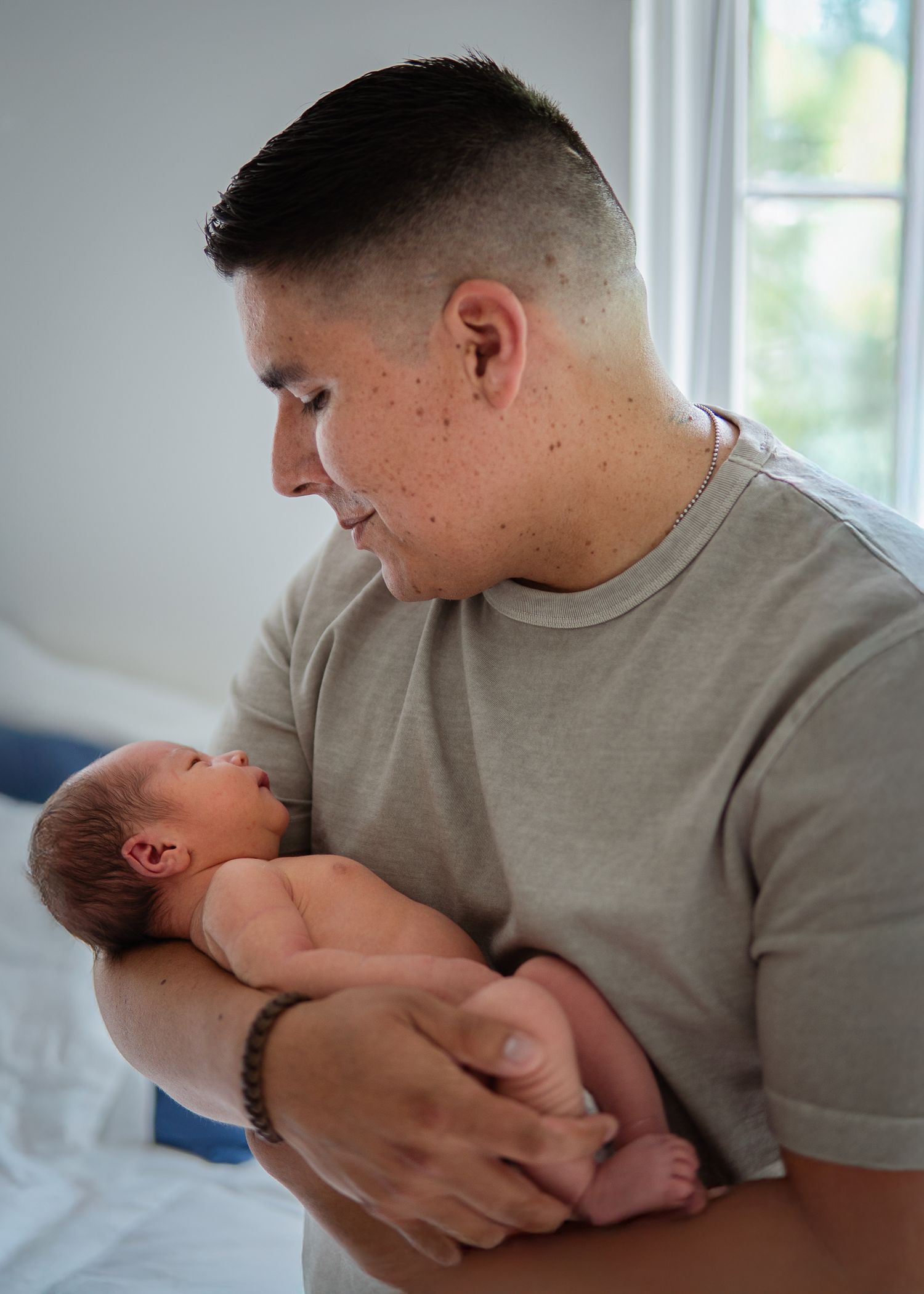 Parent in gray t-shirt gently holding and gazing at newborn baby.