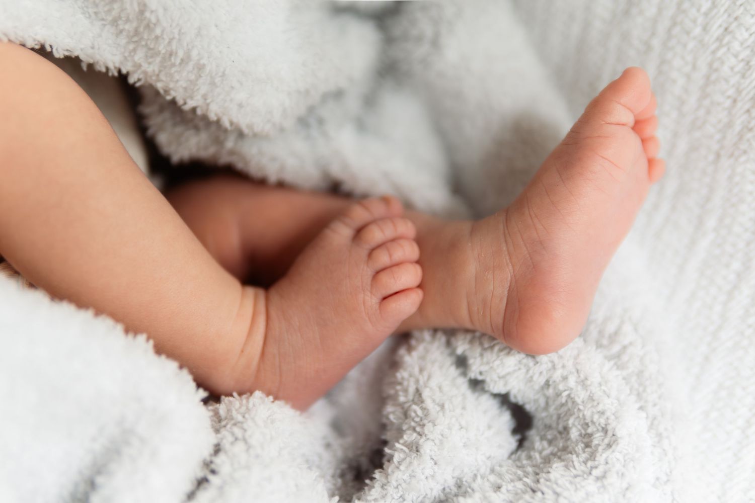 Tender detail shots of tiny newborn baby feet nestled in soft white blankets.