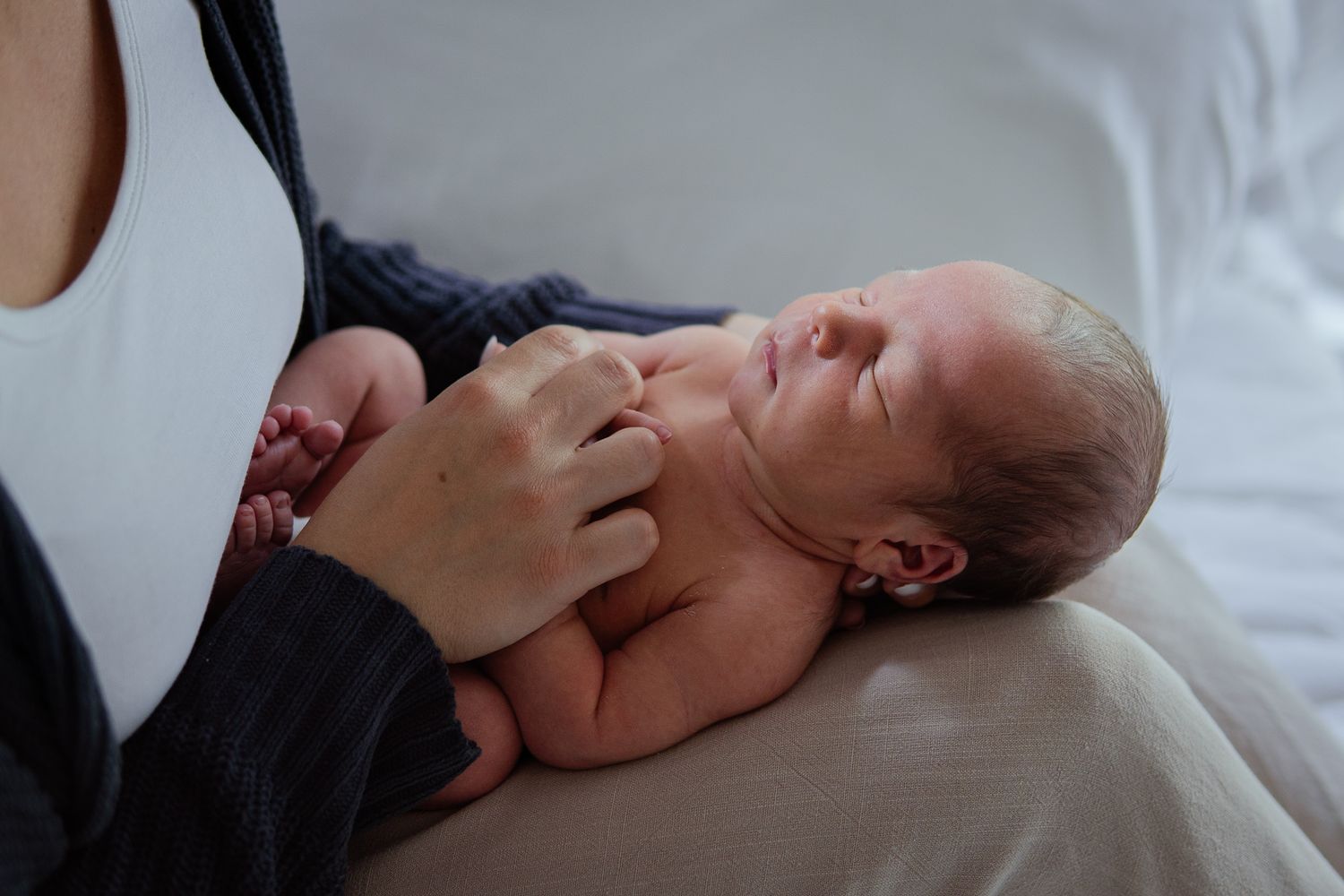 Peaceful newborn resting on caregiver's lap in natural light setting.