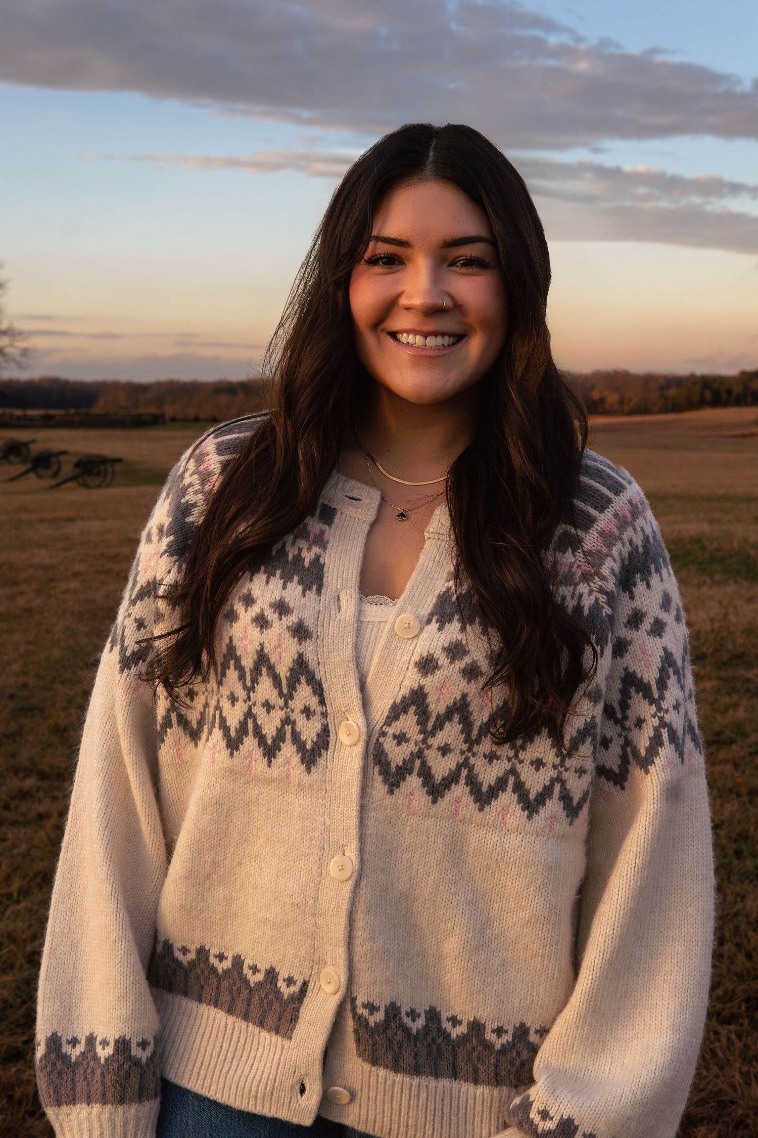 Smiling young woman in cozy Nordic cardigan posing in golden field at sunset.