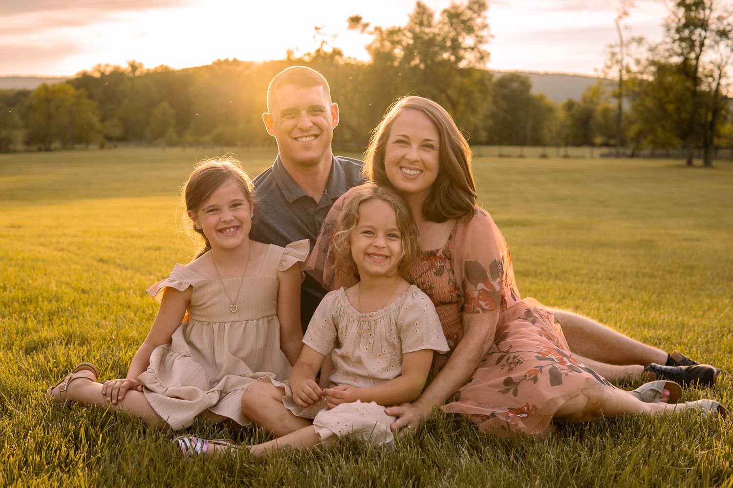 A family of five sitting together on grass in golden sunlight during sunset.