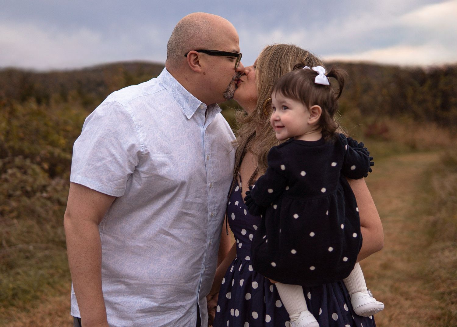 Father kissing his young daughter on the cheek while holding her on a scenic outdoor path.
