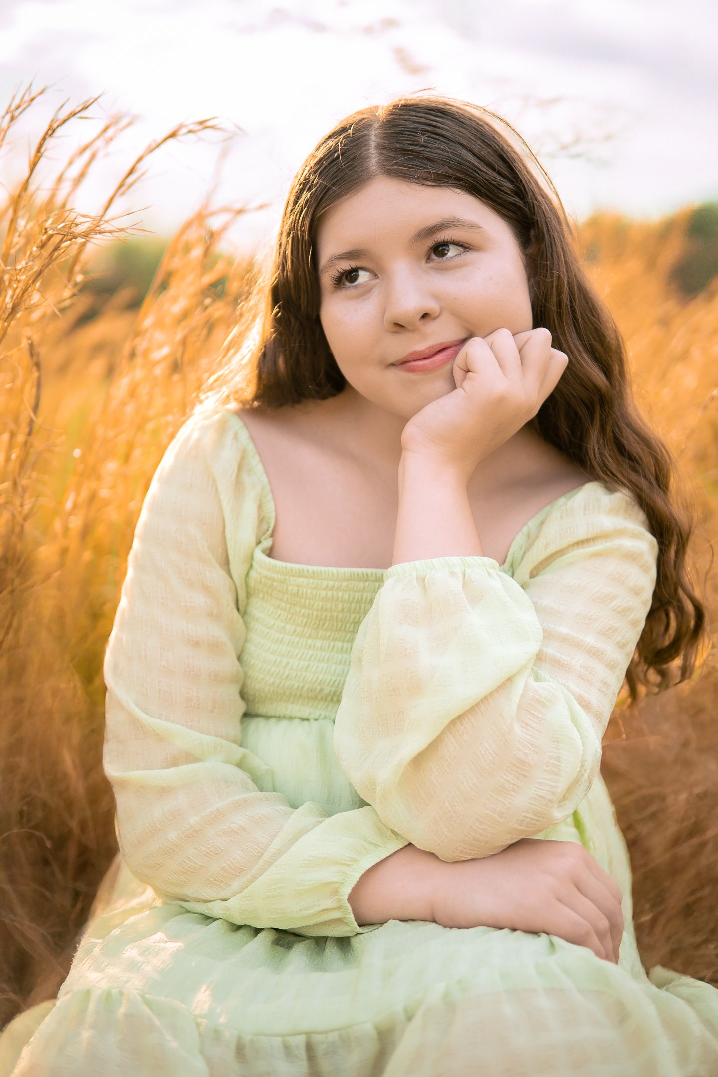 Dreamy portrait in a yellow dress sitting among golden wheat fields at sunset.