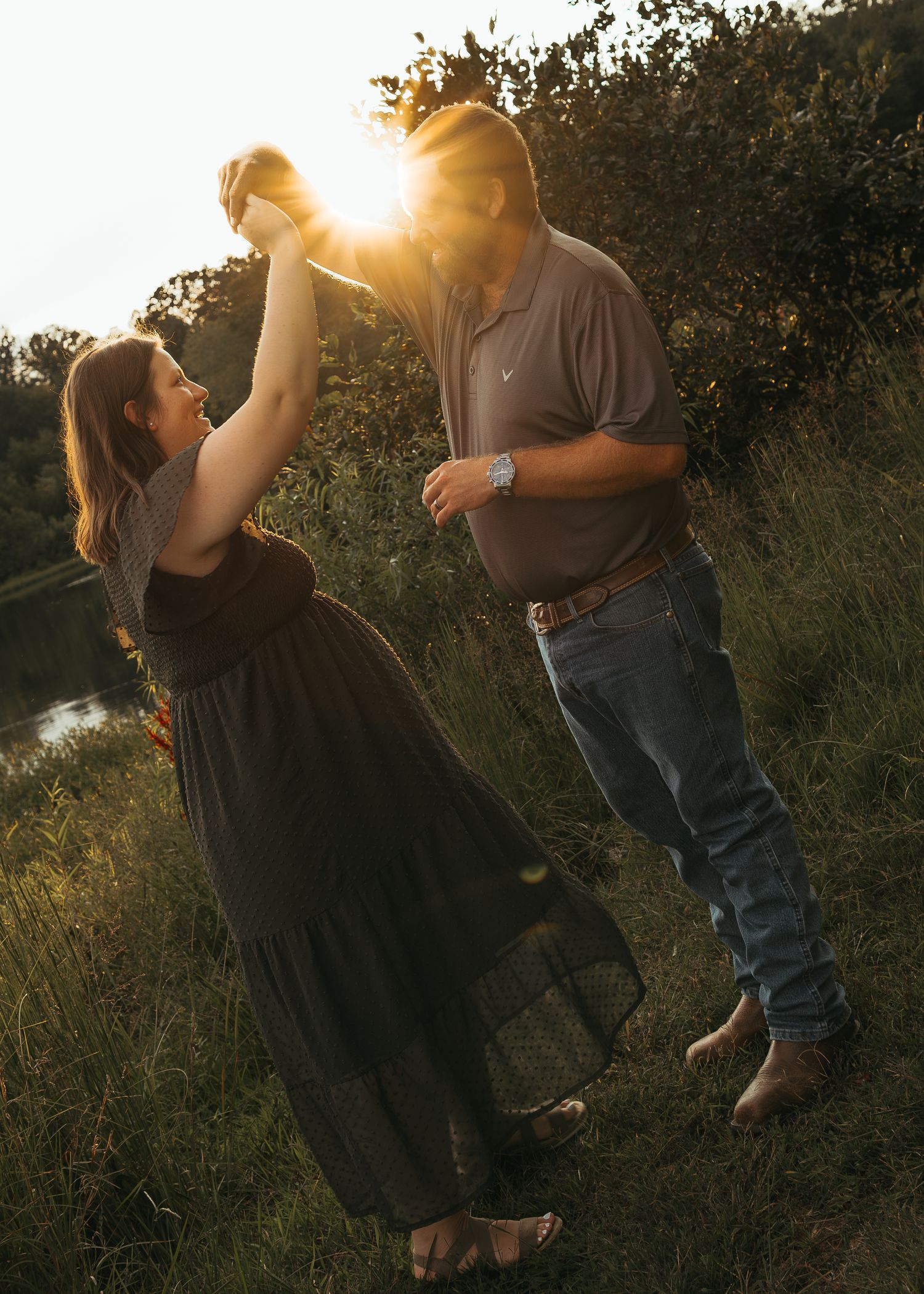 Couple dancing at golden hour sunset in a field, pregnant woman in black dress twirling.
