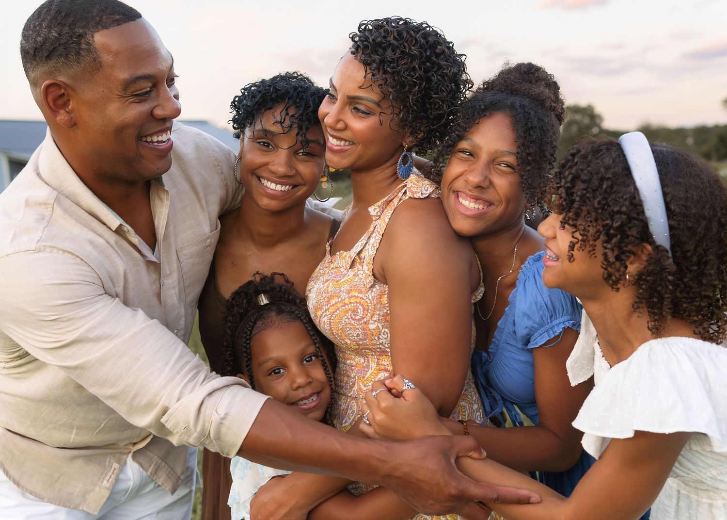 A happy Black family of six smiles and embraces together during a golden hour outdoor photo session.