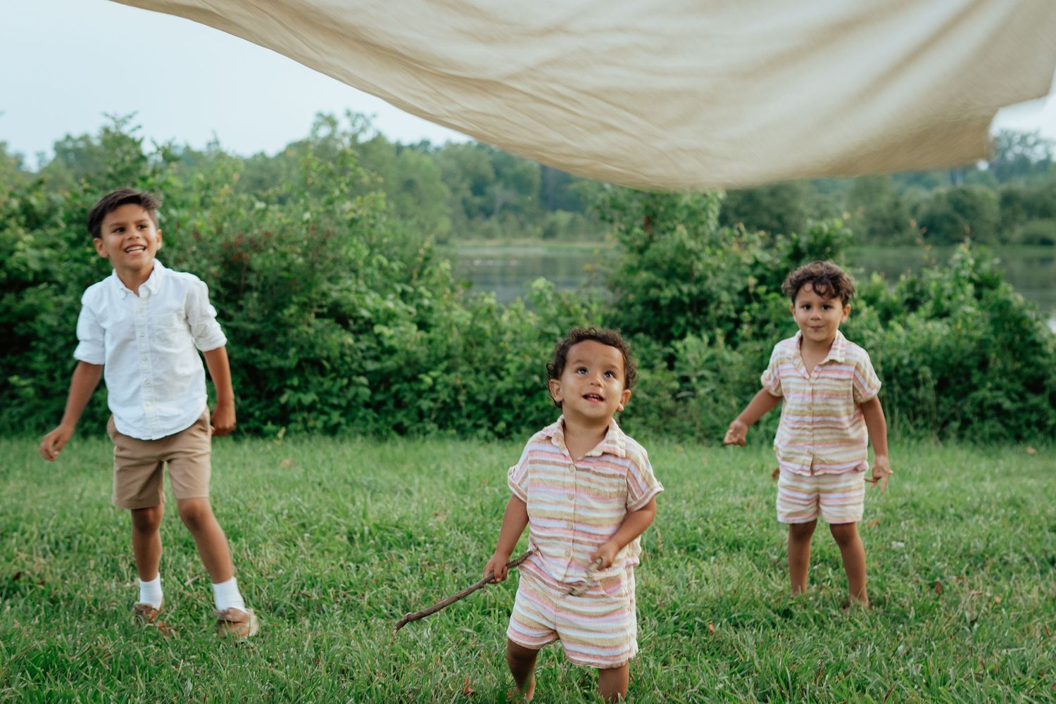 Three children playing and running under a canopy outdoors.