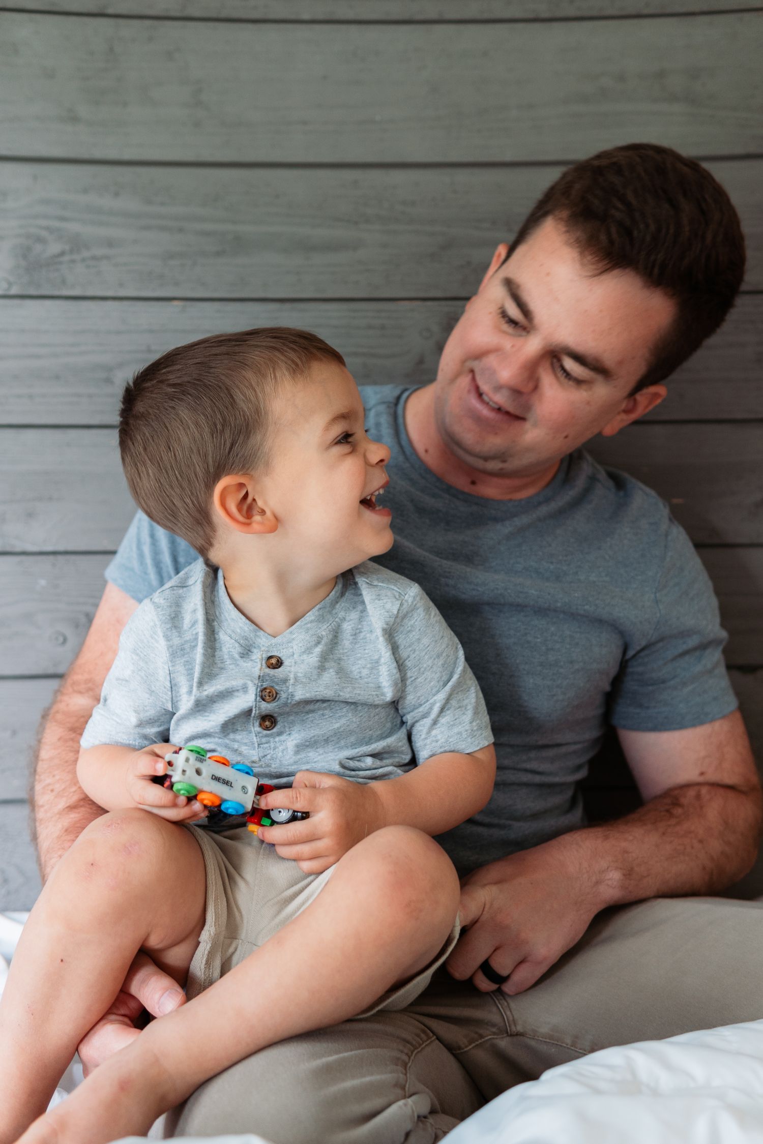 A heartwarming moment between parent and child sharing laughter while playing with a toy against a rustic wall backdrop.
