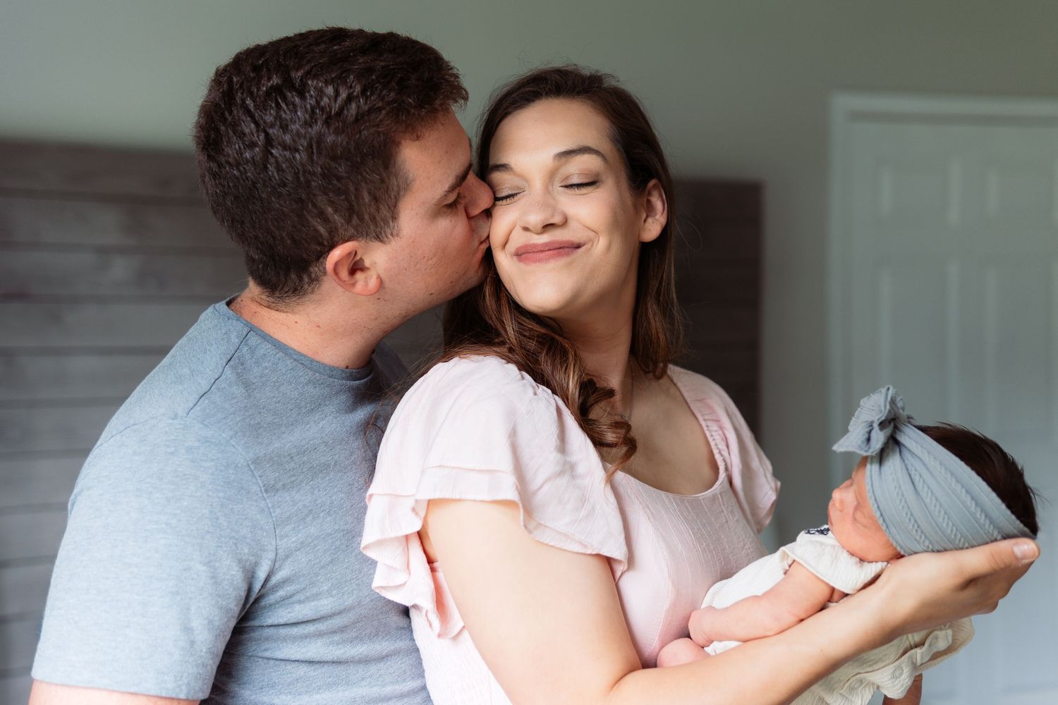 A couple shares a tender moment while holding their newborn baby wrapped in a blue blanket.