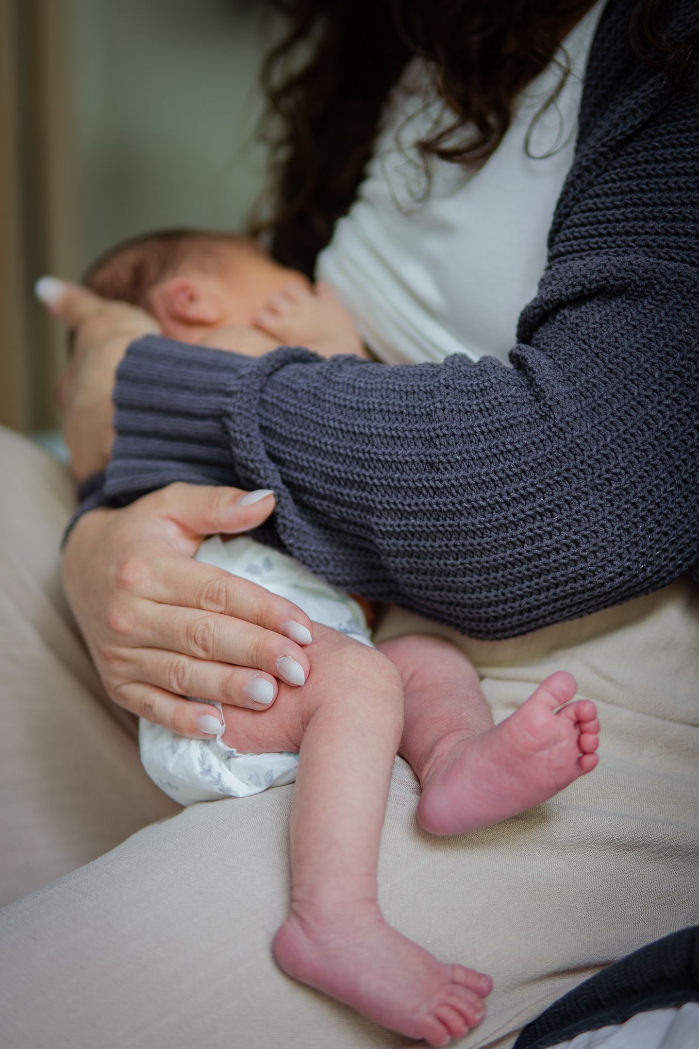 Baby's tiny feet and legs resting on caregiver's lap with gray sweater.