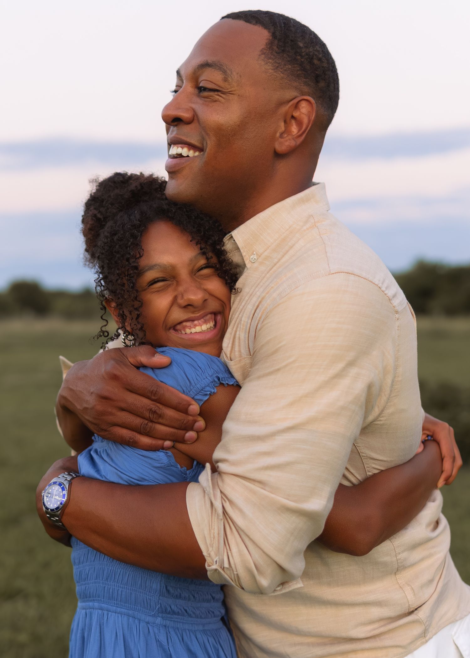 A joyful father and daughter share a warm embrace while laughing together during an outdoor family portrait session.