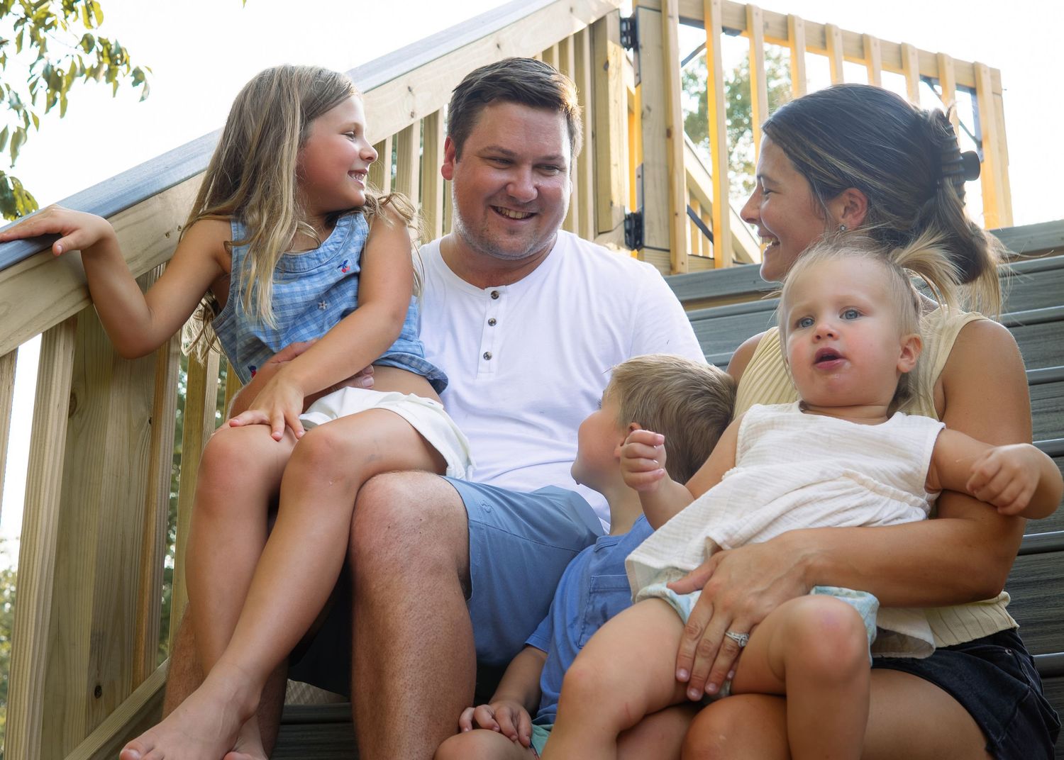 Happy family of five sitting together on wooden deck steps outdoors.