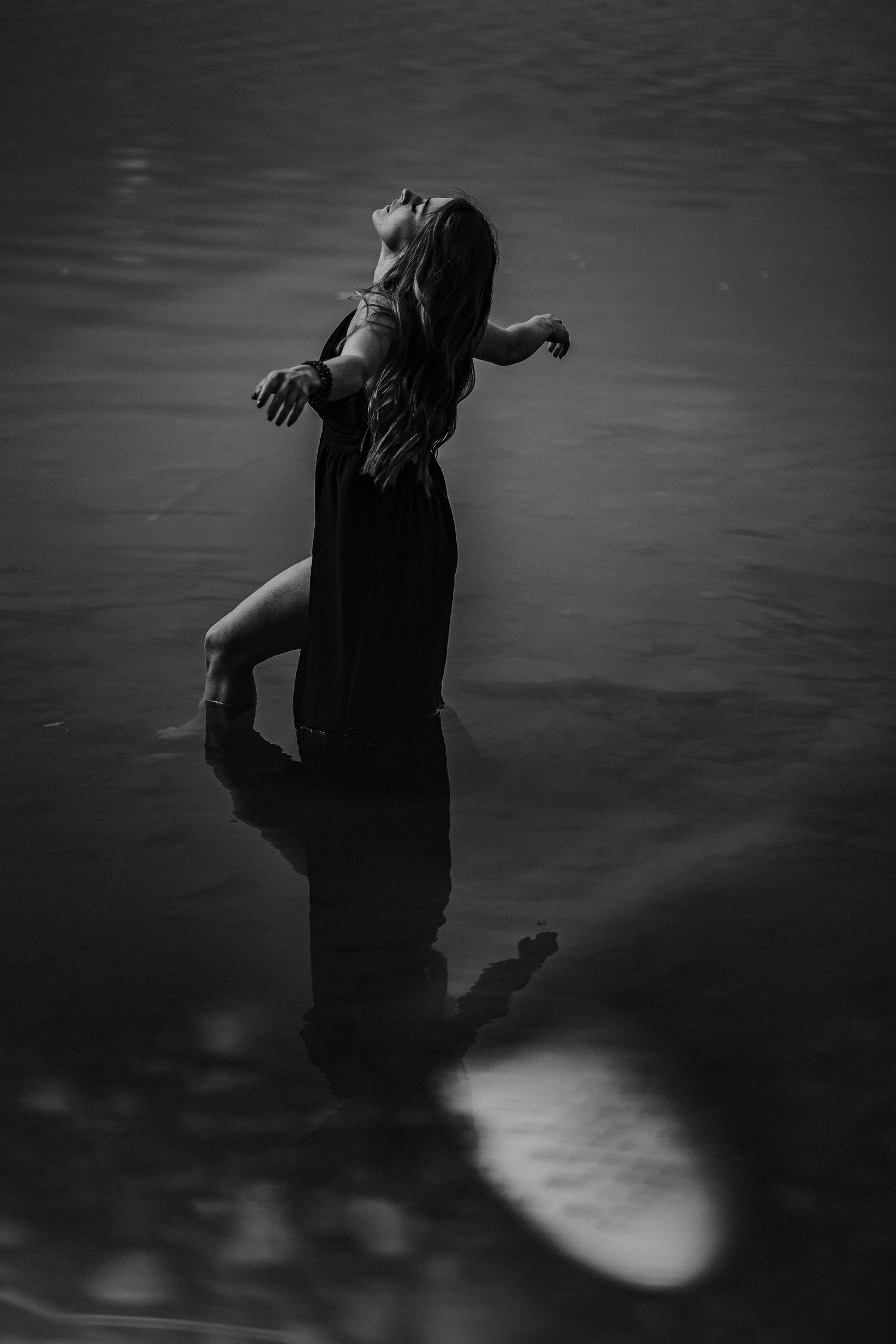 A dark and moody artistic black and white photograph showing a silhouetted figure against the water.