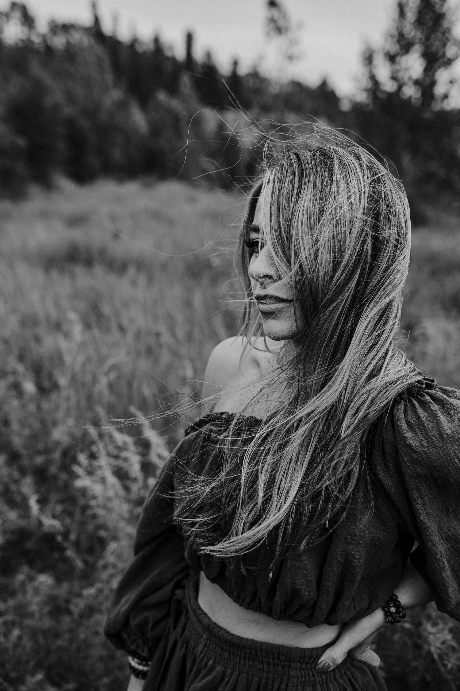 A moody black and white portrait series showing long windswept hair against a natural outdoor background.