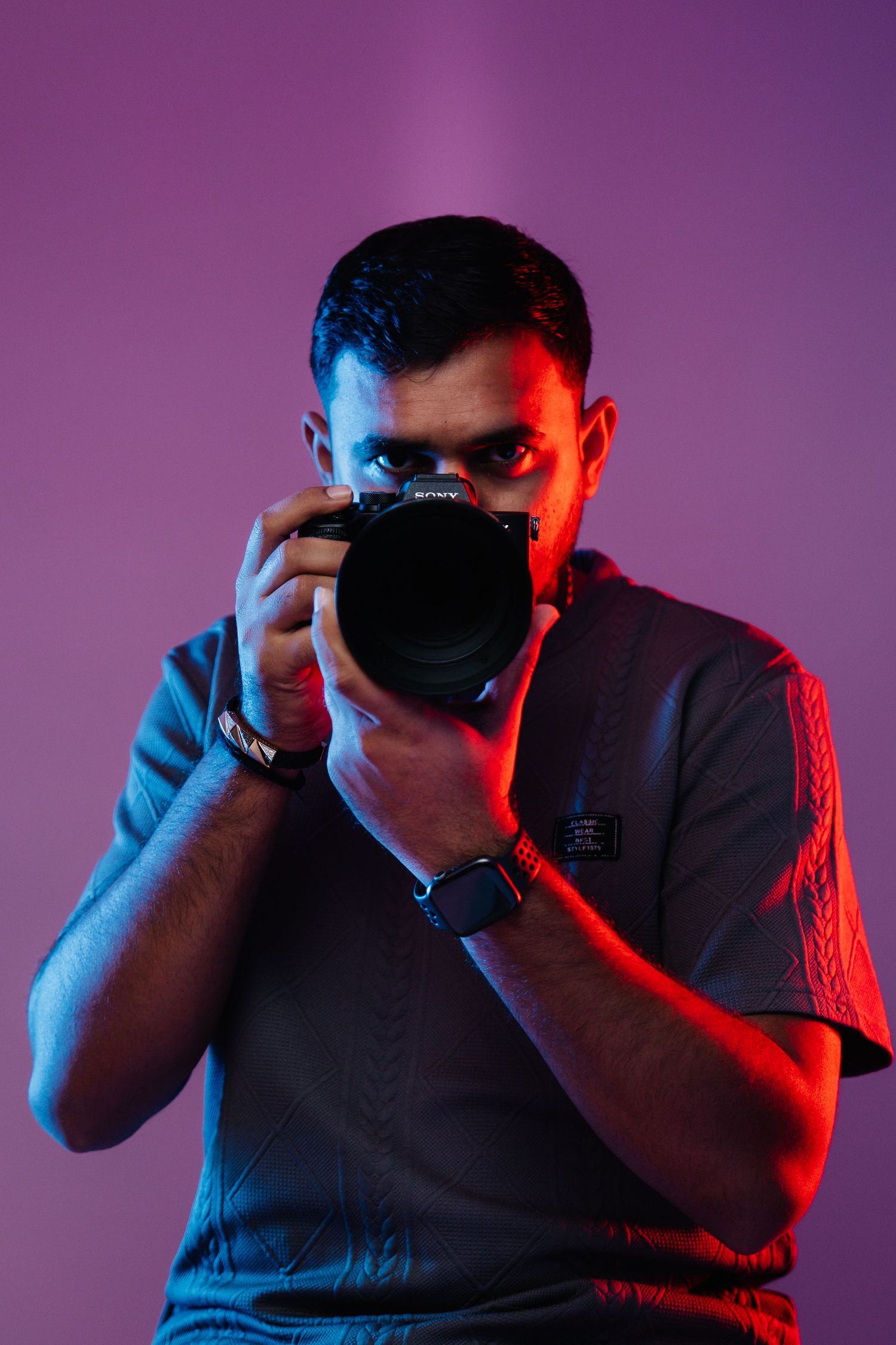 Dramatic portrait of photographer with camera against purple background lit with red and blue lights.
