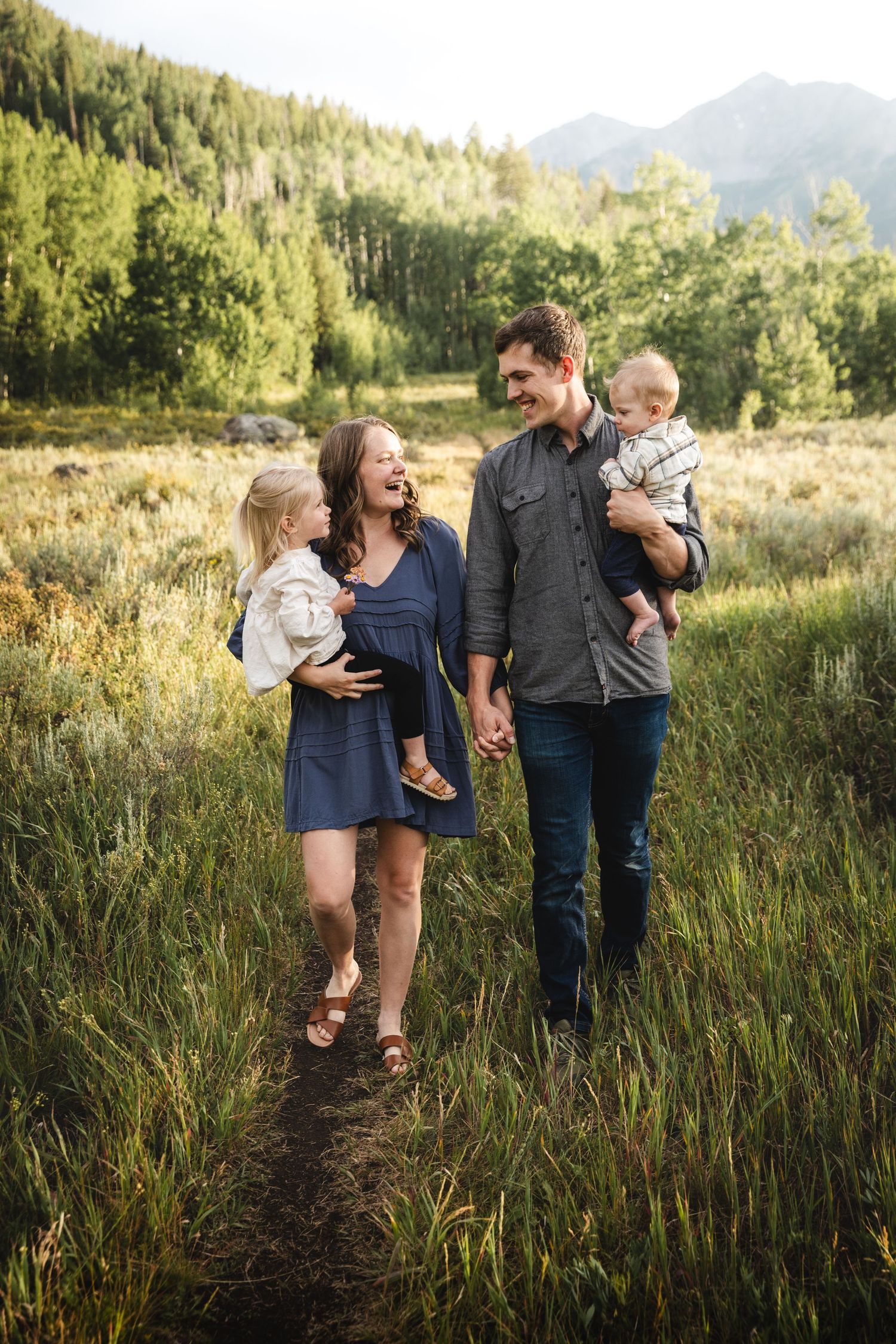 A family walks together through a sunlit meadow with tall grass and mountains in the background on a summer evening. - Frisco - Vail