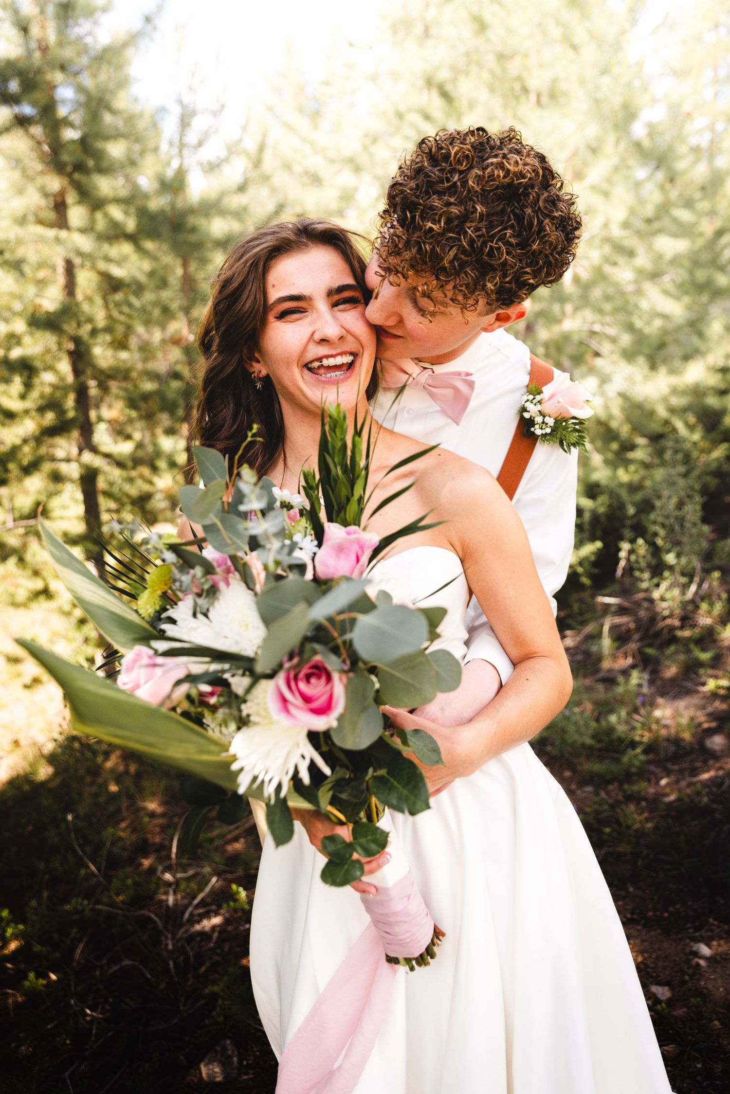 Joyful wedding moment with couple holding floral bouquet in forest setting.