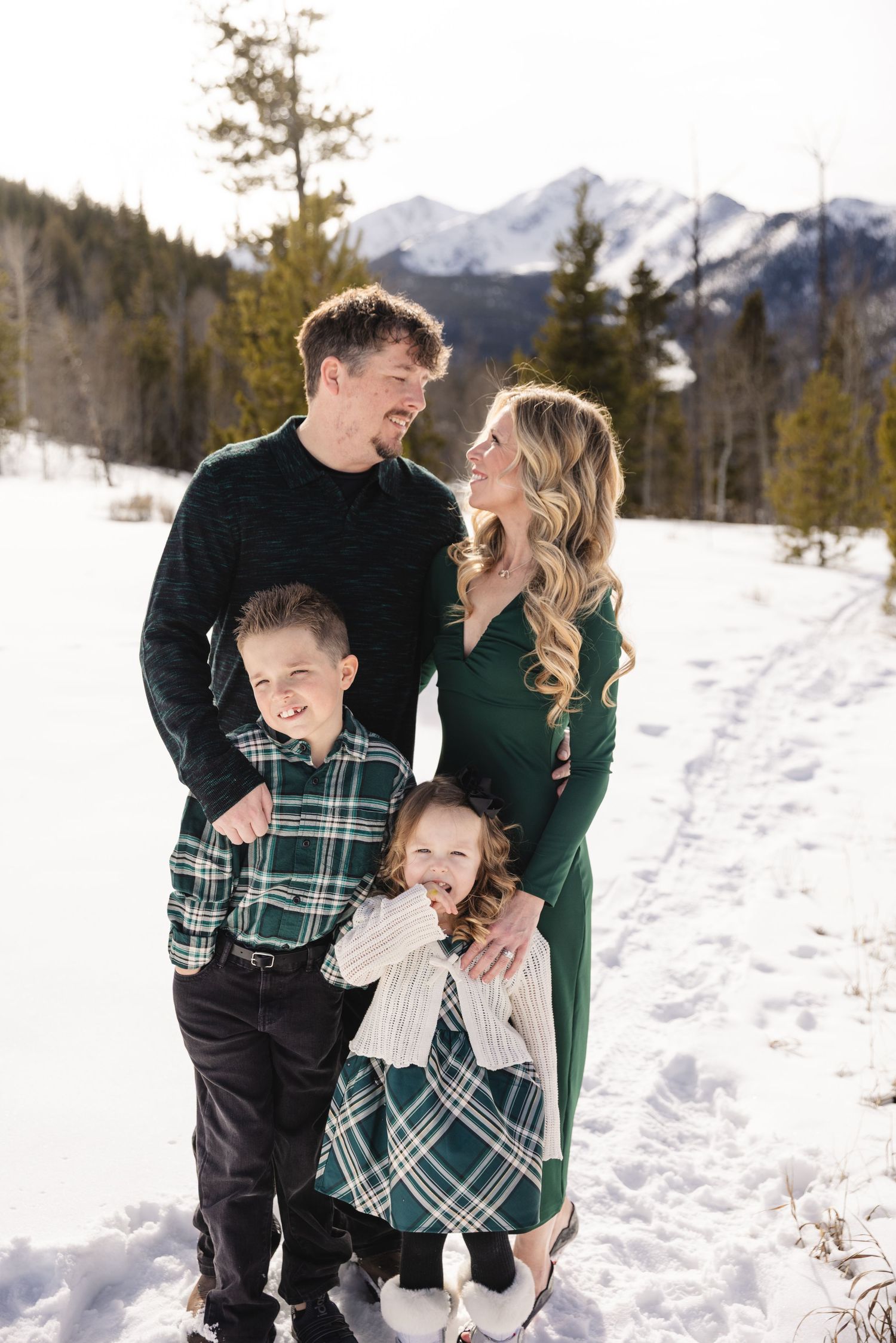 Family of four posing in snowy mountain landscape, wearing coordinated green outfits, smiling together outdoors in winter. - silverthorne