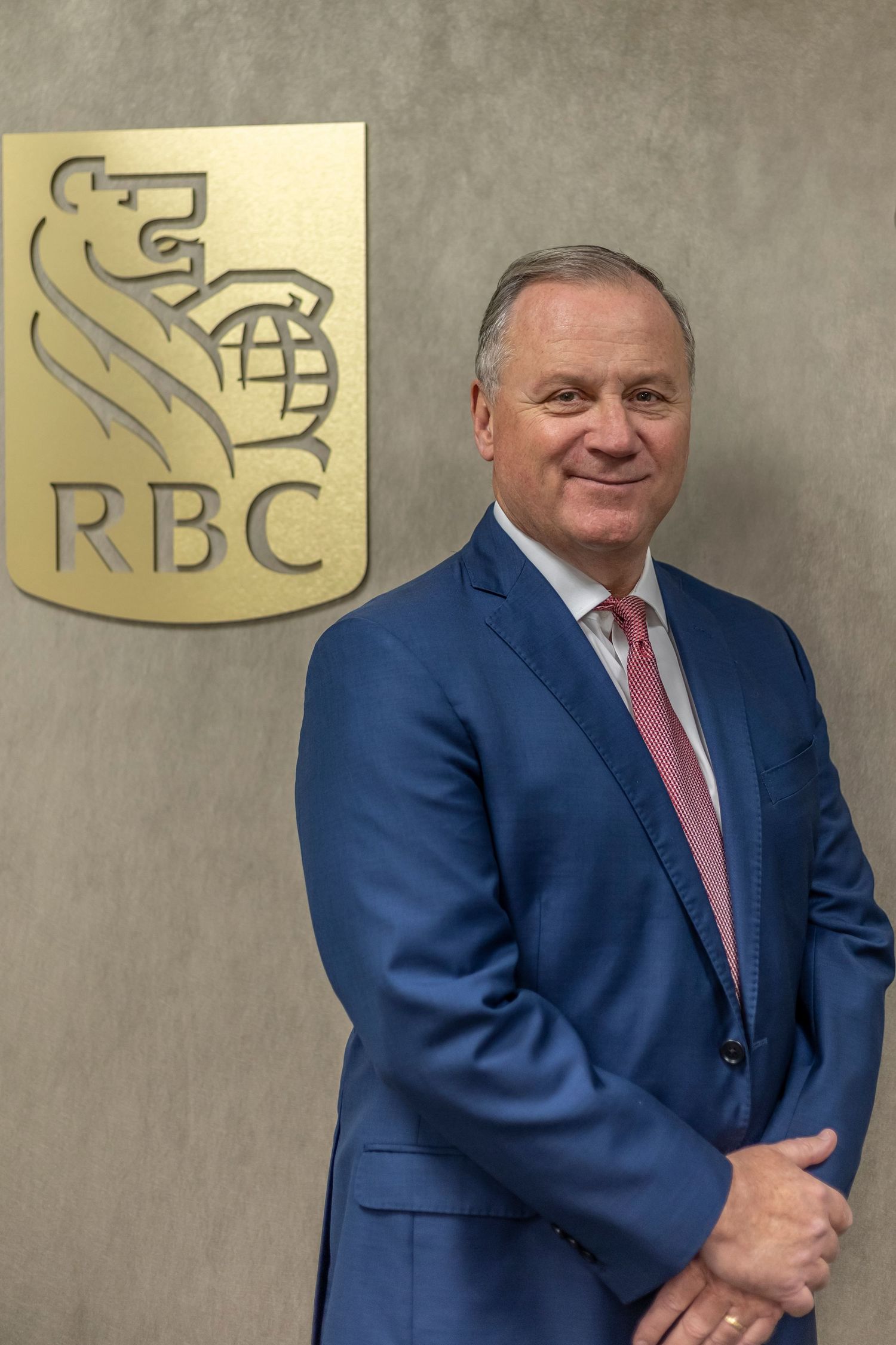 Professional portrait of a person in a navy blue suit and pink tie standing next to the gold RBC bank logo.