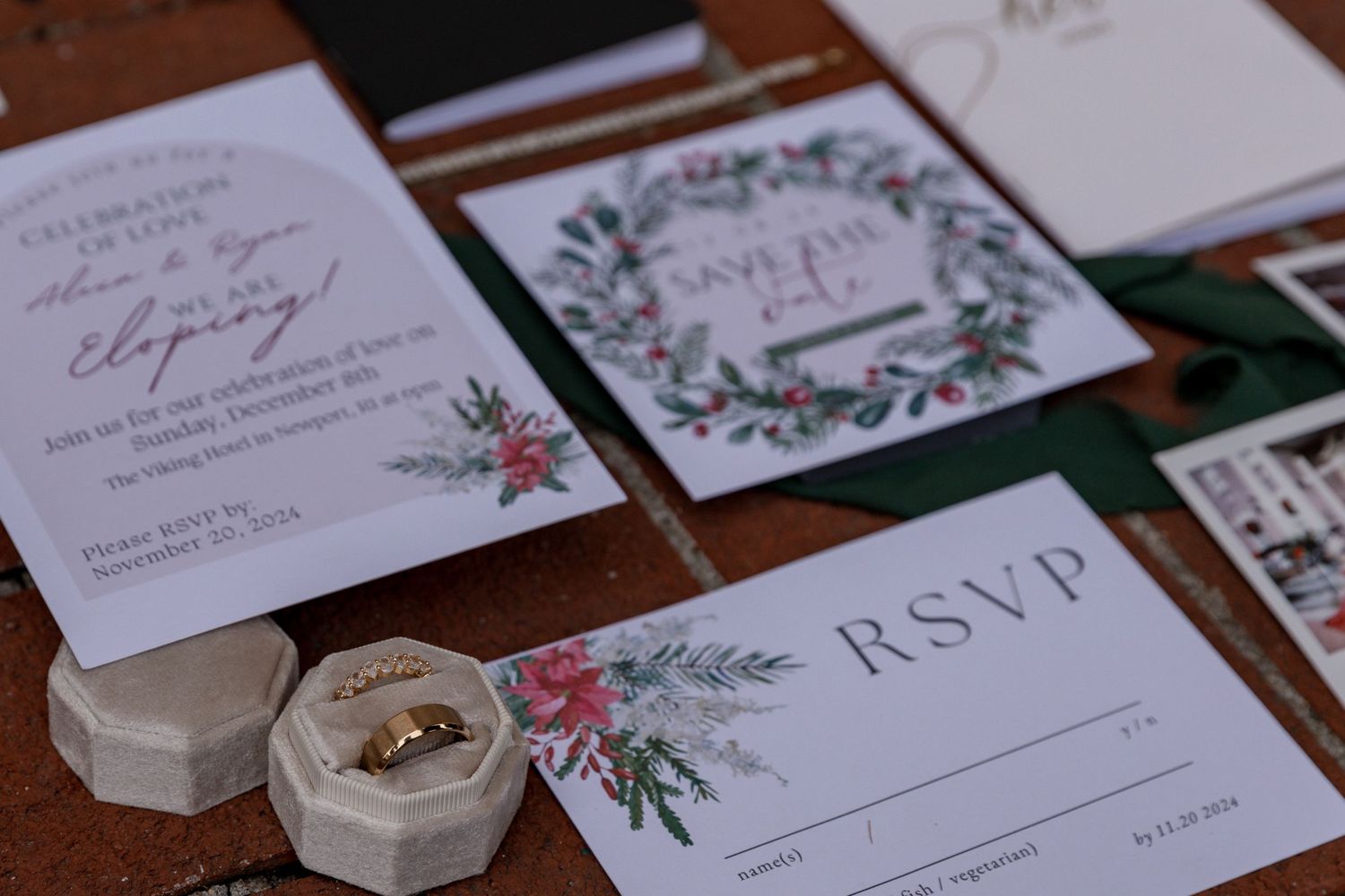 Wedding invitation suite with floral designs and RSVP card displayed alongside gold wedding rings in clear box.