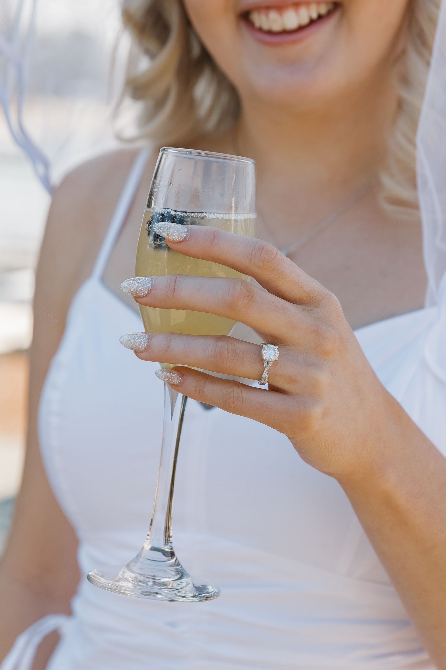 Close-up of a champagne glass being held by a hand wearing an elegant engagement ring.