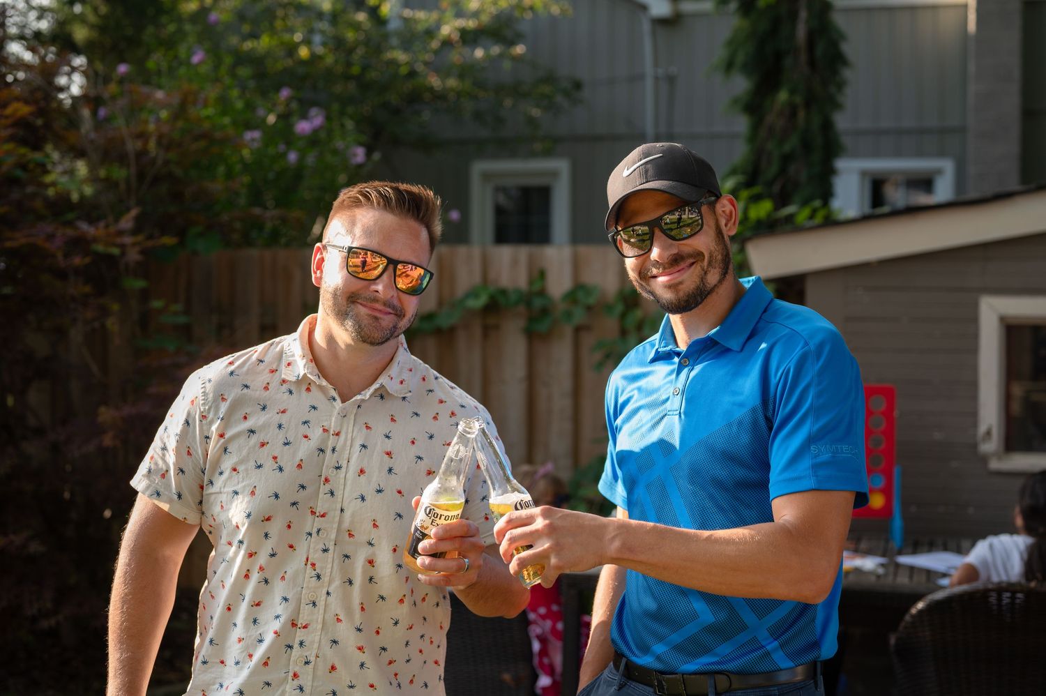Two friends sharing drinks and smiling in outdoor backyard setting.