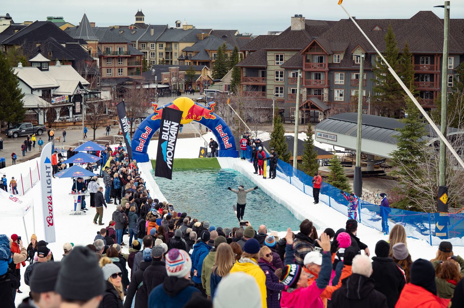 Crowd watching winter sports event with inflatable arch over snow ramp at ski resort.