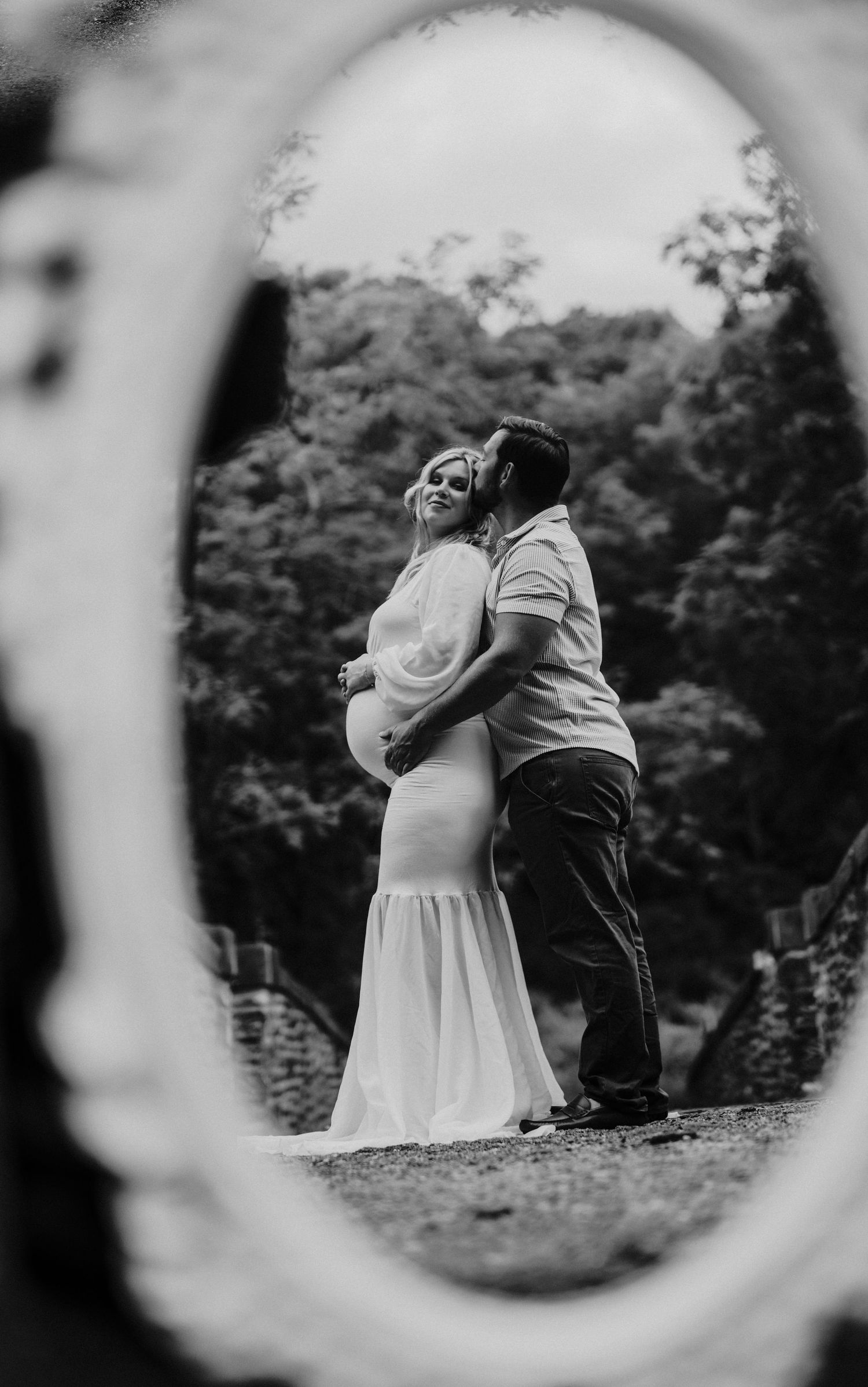 Romantic couple's silhouette viewed through a circular frame in a garden setting.
