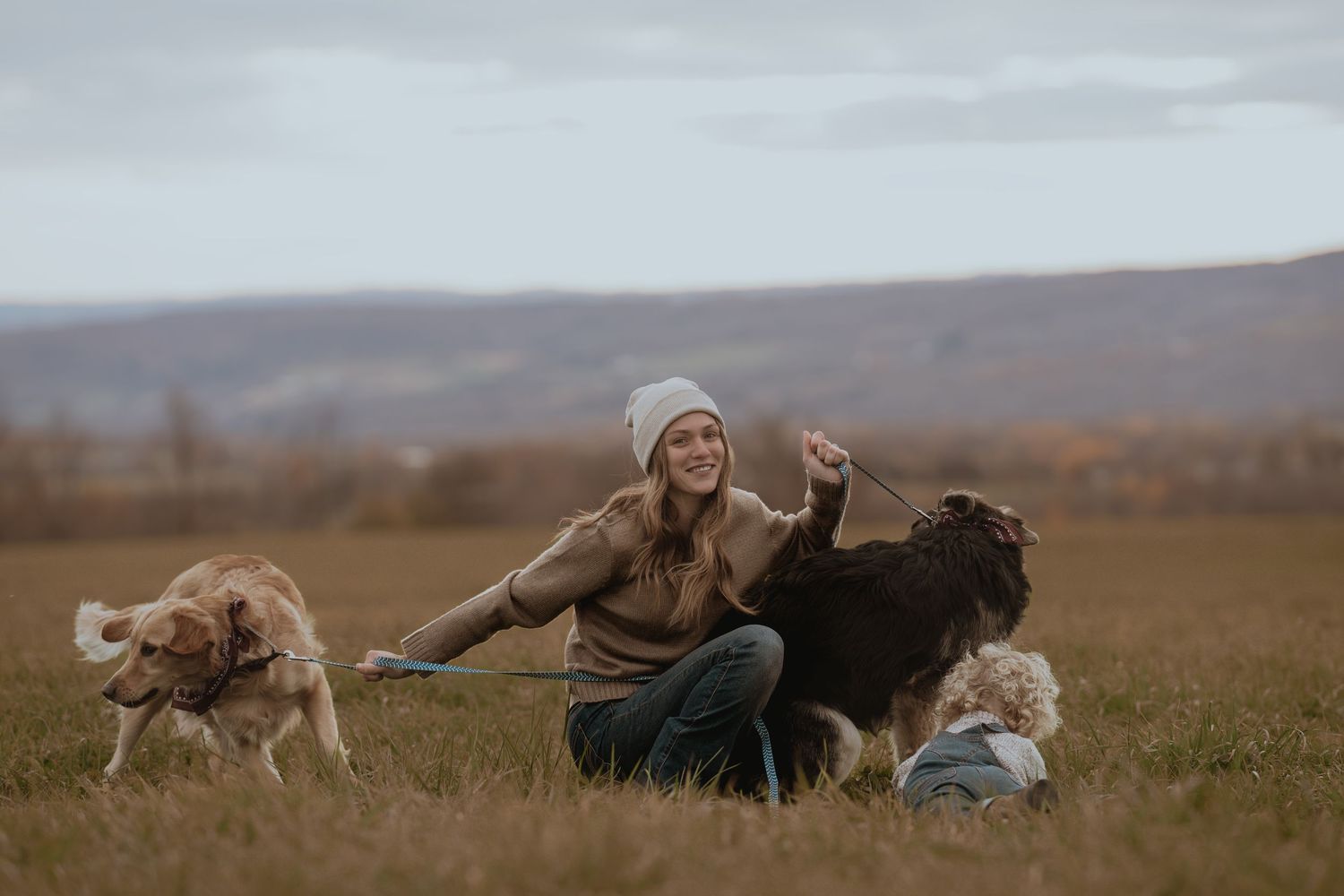 Playful scene on a grassy hillside with a dog running alongside people.