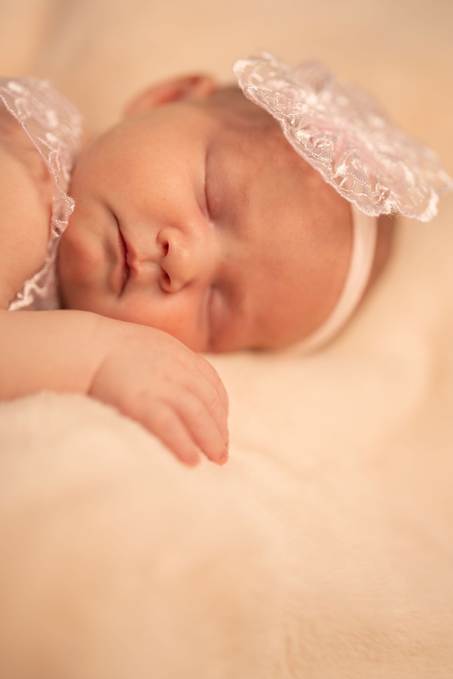 Newborn baby sleeping peacefully under delicate lace fabric in warm lighting.